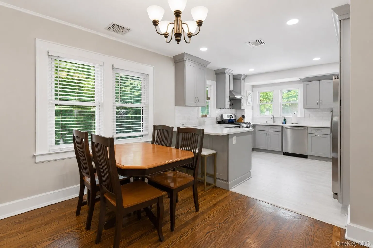 Dining area with hardwood flooring and a kitchen featuring light gray cabinetry, white countertops, and stainless steel appliances Dining area with hardwood flooring and a kitchen featuring light gray cabinetry, white countertops, and stainless steel appliances