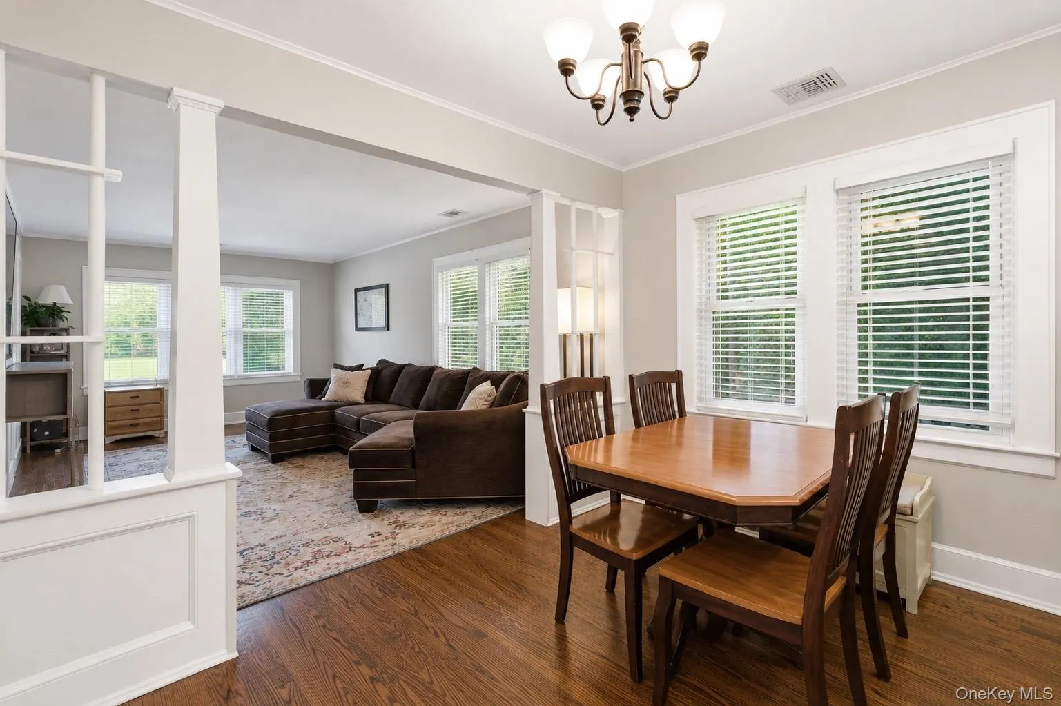Dining area featuring dark wood-finish flooring, a traditional chandelier, multiple windows with blinds, and white trim molding Dining area featuring dark wood-finish flooring, a traditional chandelier, multiple windows with blinds, and white trim molding