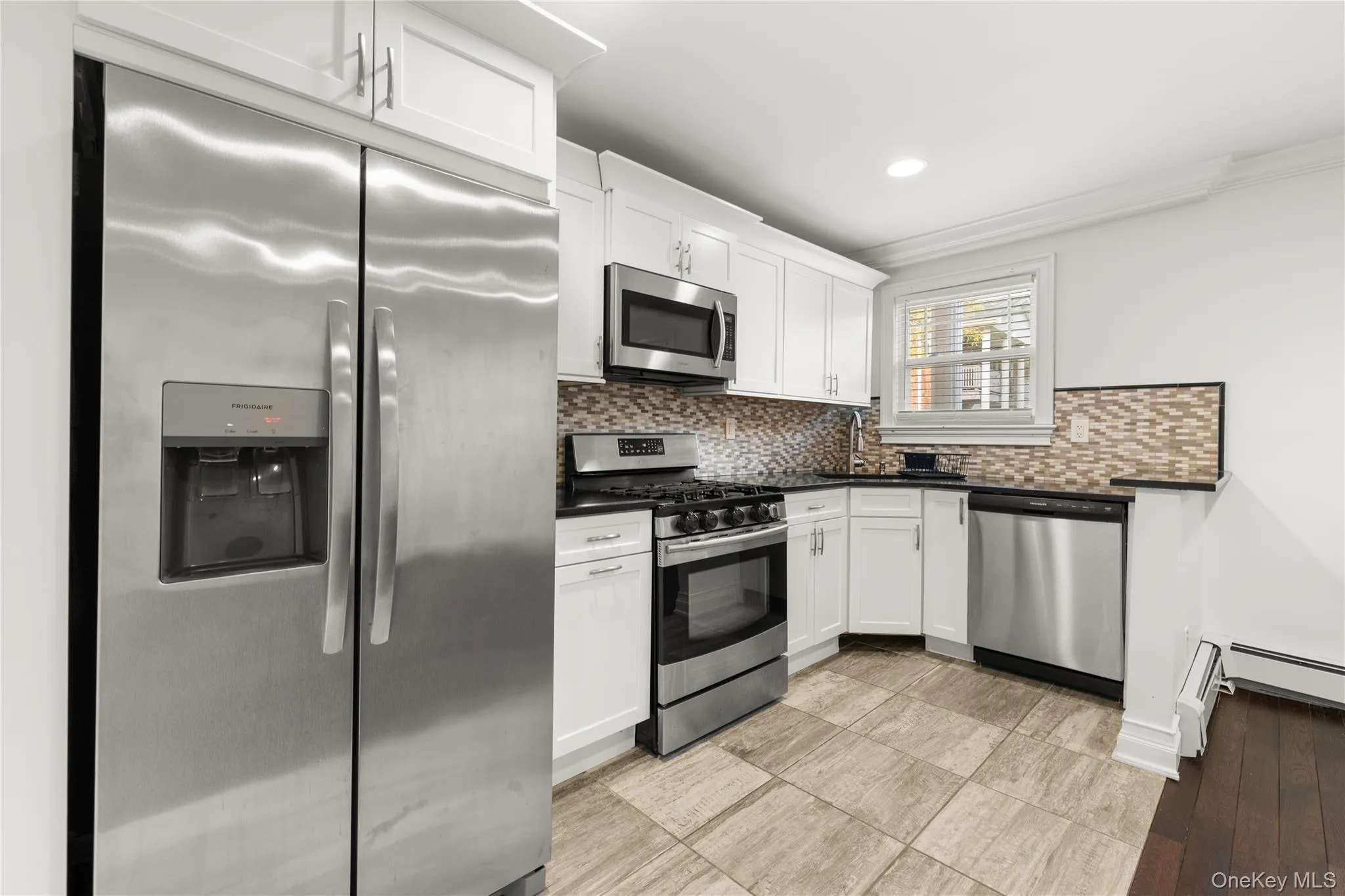 Kitchen with stainless steel appliances, backsplash, white cabinets, and light matching flooring Kitchen with stainless steel appliances, backsplash, white cabinets, and light matching flooring