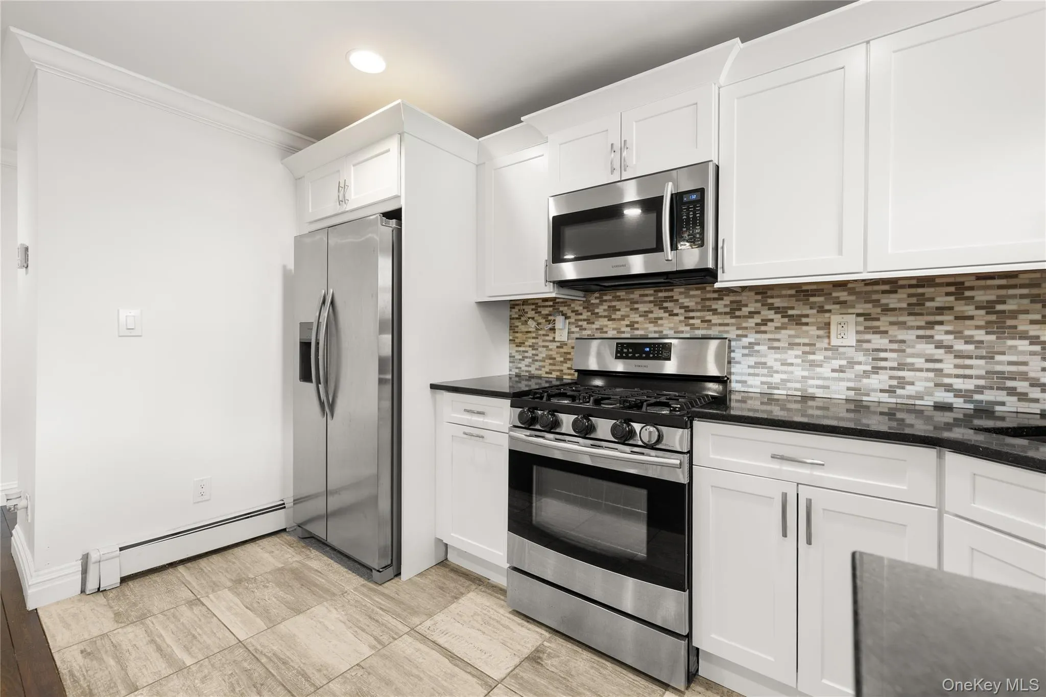 Kitchen view of decorative backsplash, dark quartz countertops, and white cabinetry Kitchen view of decorative backsplash, dark quartz countertops, and white cabinetry