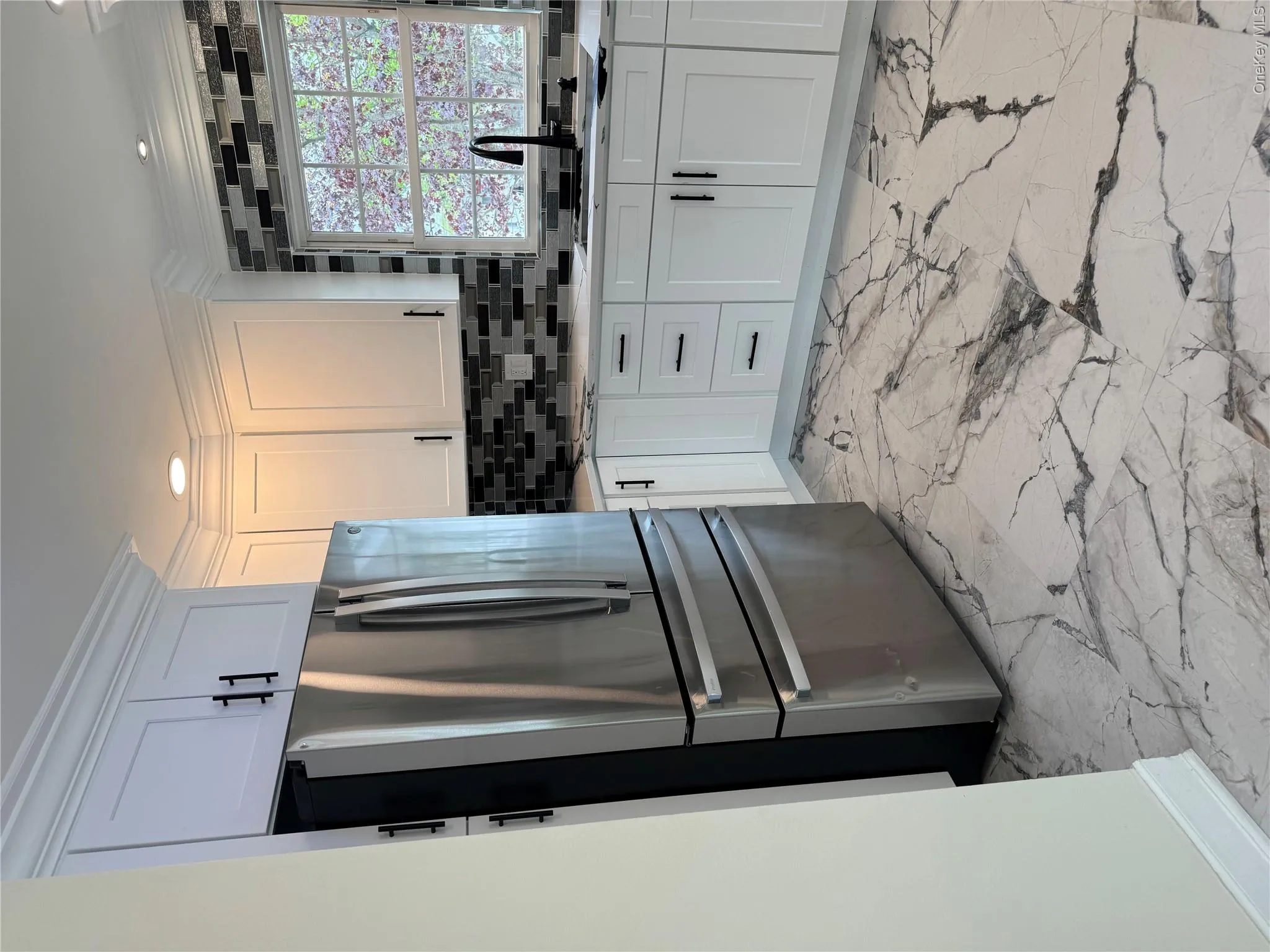 Modern kitchen featuring white shaker cabinetry with matte black hardware, a stainless steel French door refrigerator, and a mosaic tile backsplash Modern kitchen featuring white shaker cabinetry with matte black hardware, a stainless steel French door refrigerator, and a mosaic tile backsplash