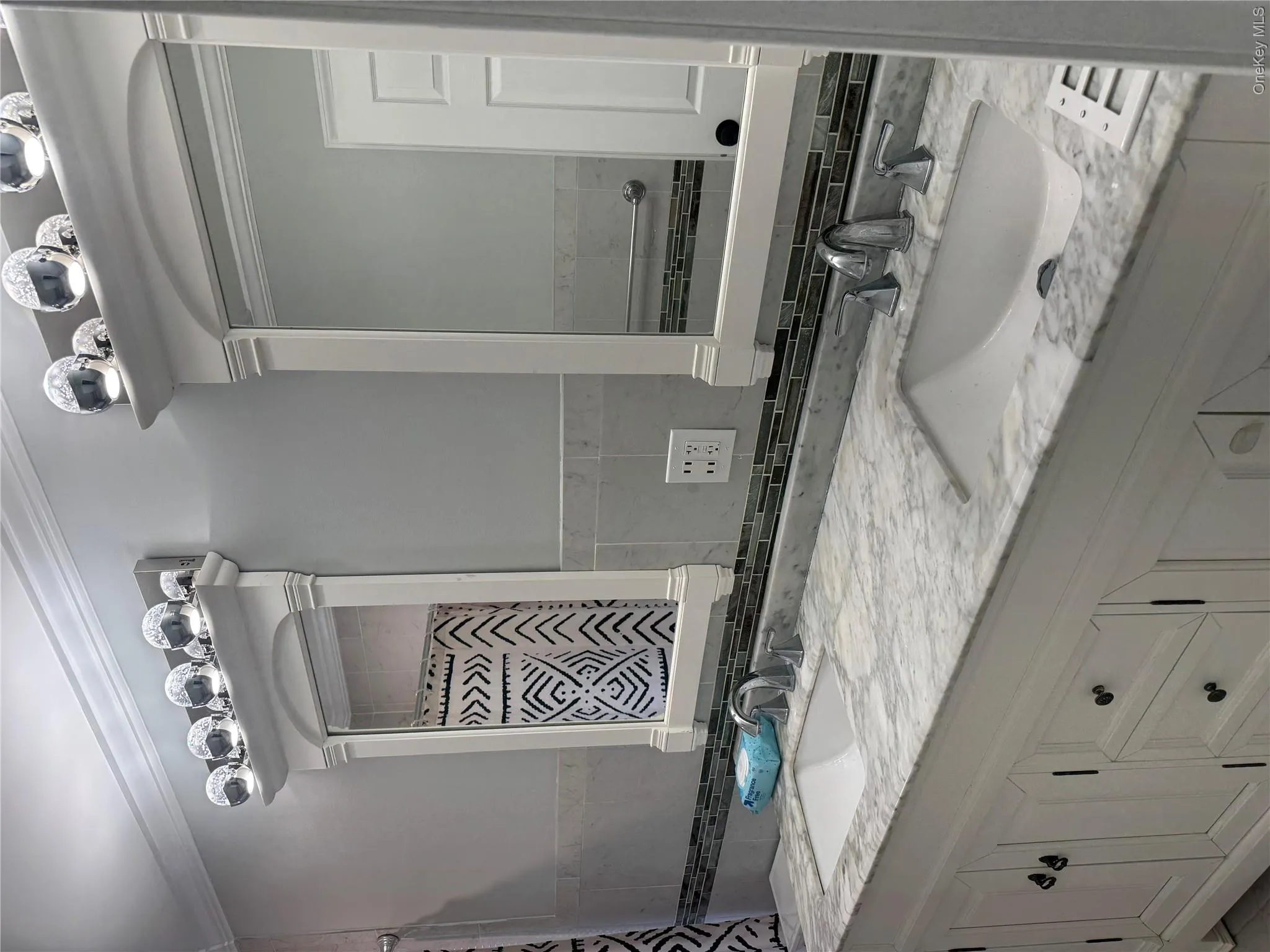 Double vanity featuring white cabinetry, integrated sinks, a patterned countertop, and a mosaic tile backsplash Double vanity featuring white cabinetry, integrated sinks, a patterned countertop, and a mosaic tile backsplash