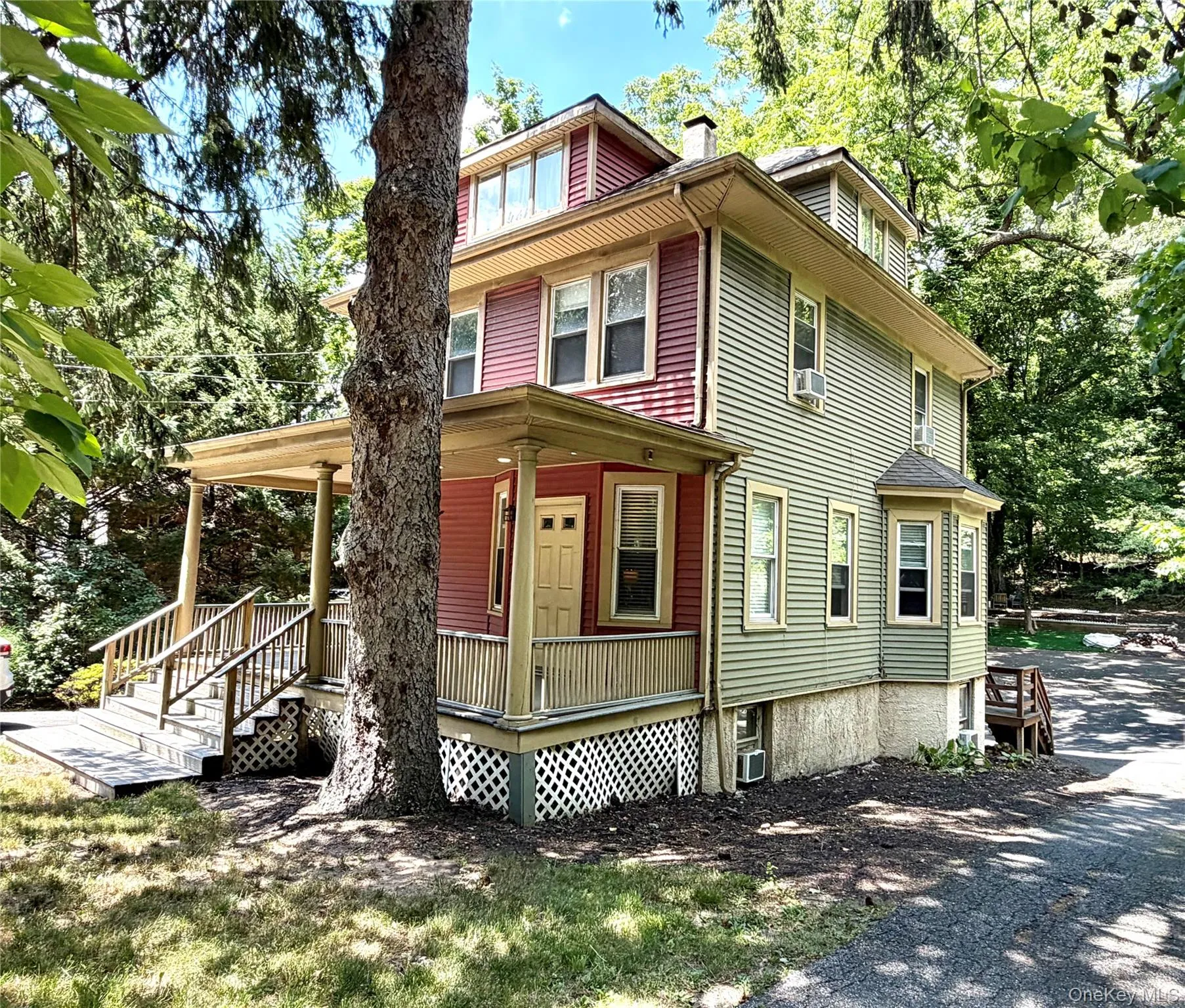 Multi-level residential property with red and sage green siding, featuring a covered front porch with lattice detailing Multi-level residential property with red and sage green siding, featuring a covered front porch with lattice detailing