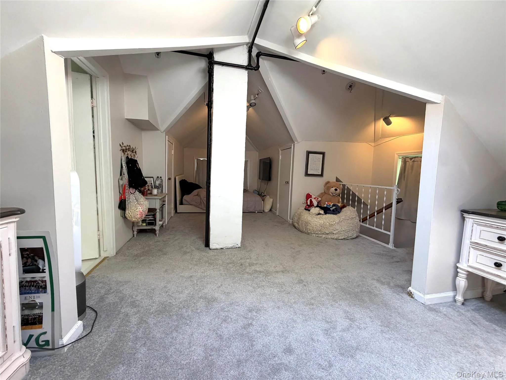 Carpeted loft area featuring sloped ceilings, track lighting, white painted trim, and a white baluster railing Carpeted loft area featuring sloped ceilings, track lighting, white painted trim, and a white baluster railing