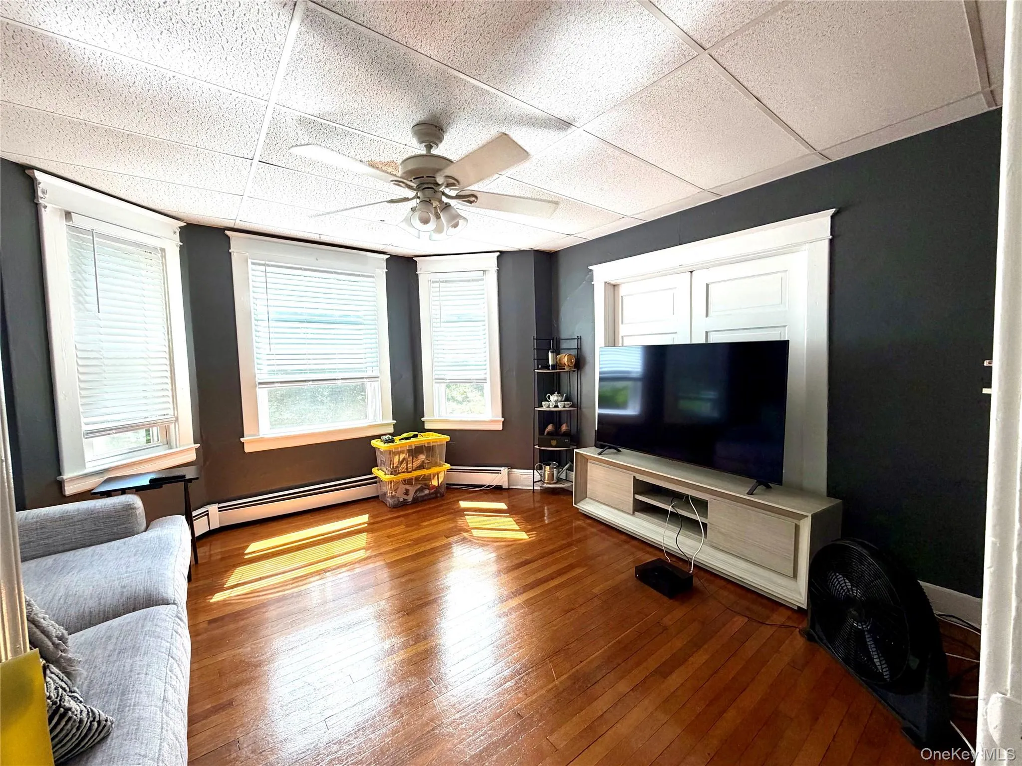 Living area featuring wood-finish flooring, a ceiling fan with integrated lighting, and multiple windows with white blinds Living area featuring wood-finish flooring, a ceiling fan with integrated lighting, and multiple windows with white blinds