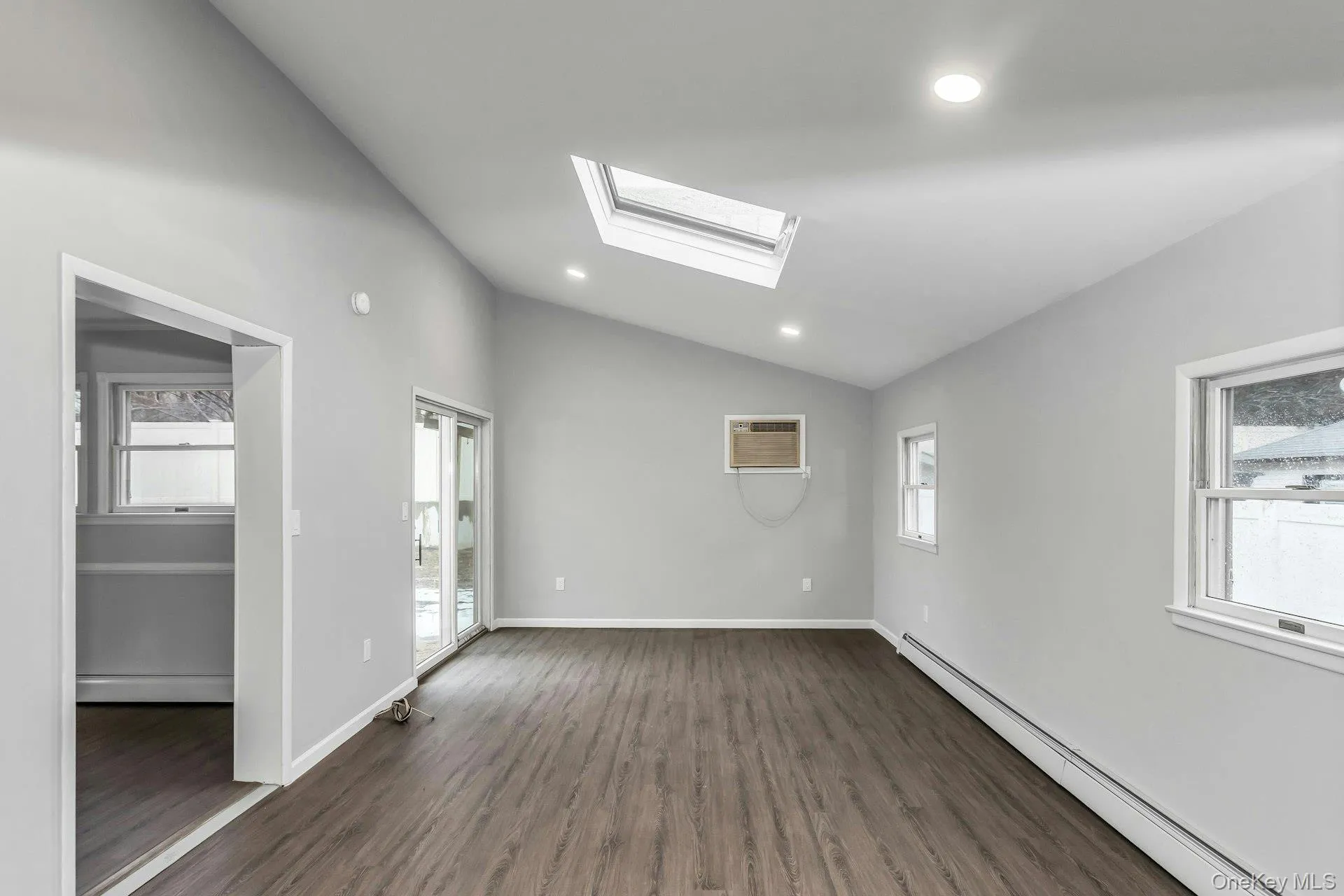 Vaulted ceiling with an integrated skylight, wood-finish flooring, recessed lighting, white baseboards, and sliding glass doors Vaulted ceiling with an integrated skylight, wood-finish flooring, recessed lighting, white baseboards, and sliding glass doors