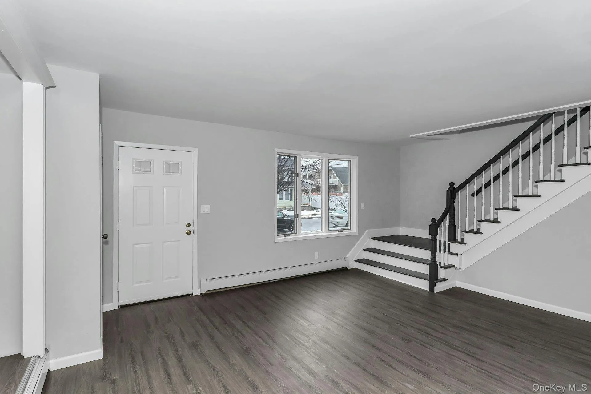 Entryway featuring wood-finish flooring, a contemporary staircase with dark wood-finish handrails and white balusters, and a paneled entry door Entryway featuring wood-finish flooring, a contemporary staircase with dark wood-finish handrails and white balusters, and a paneled entry door
