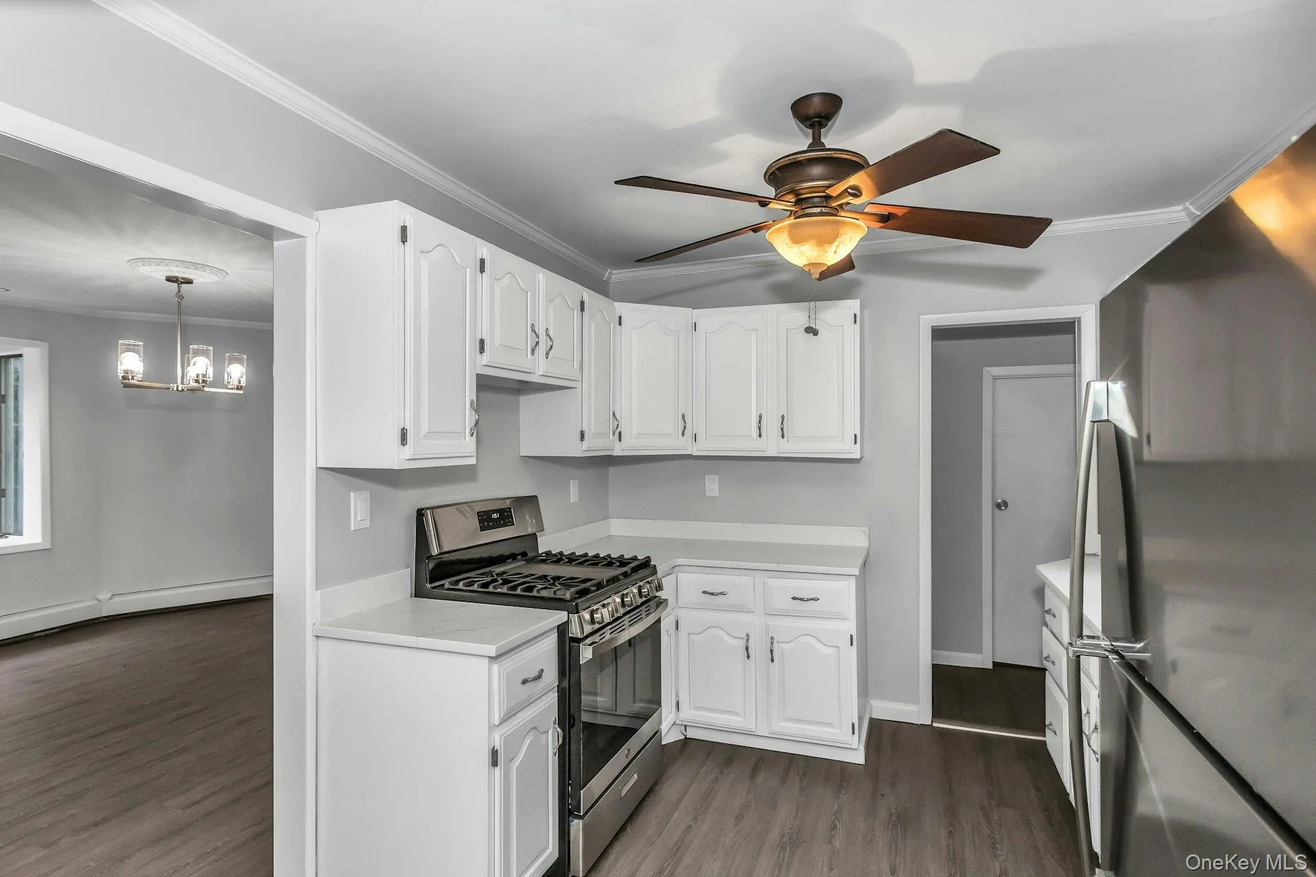 Eat-in kitchen featuring white cabinetry, light-toned countertops, stainless steel appliances, wood-finish flooring, and a ceiling fan with integrated lighting Eat-in kitchen featuring white cabinetry, light-toned countertops, stainless steel appliances, wood-finish flooring, and a ceiling fan with integrated lighting