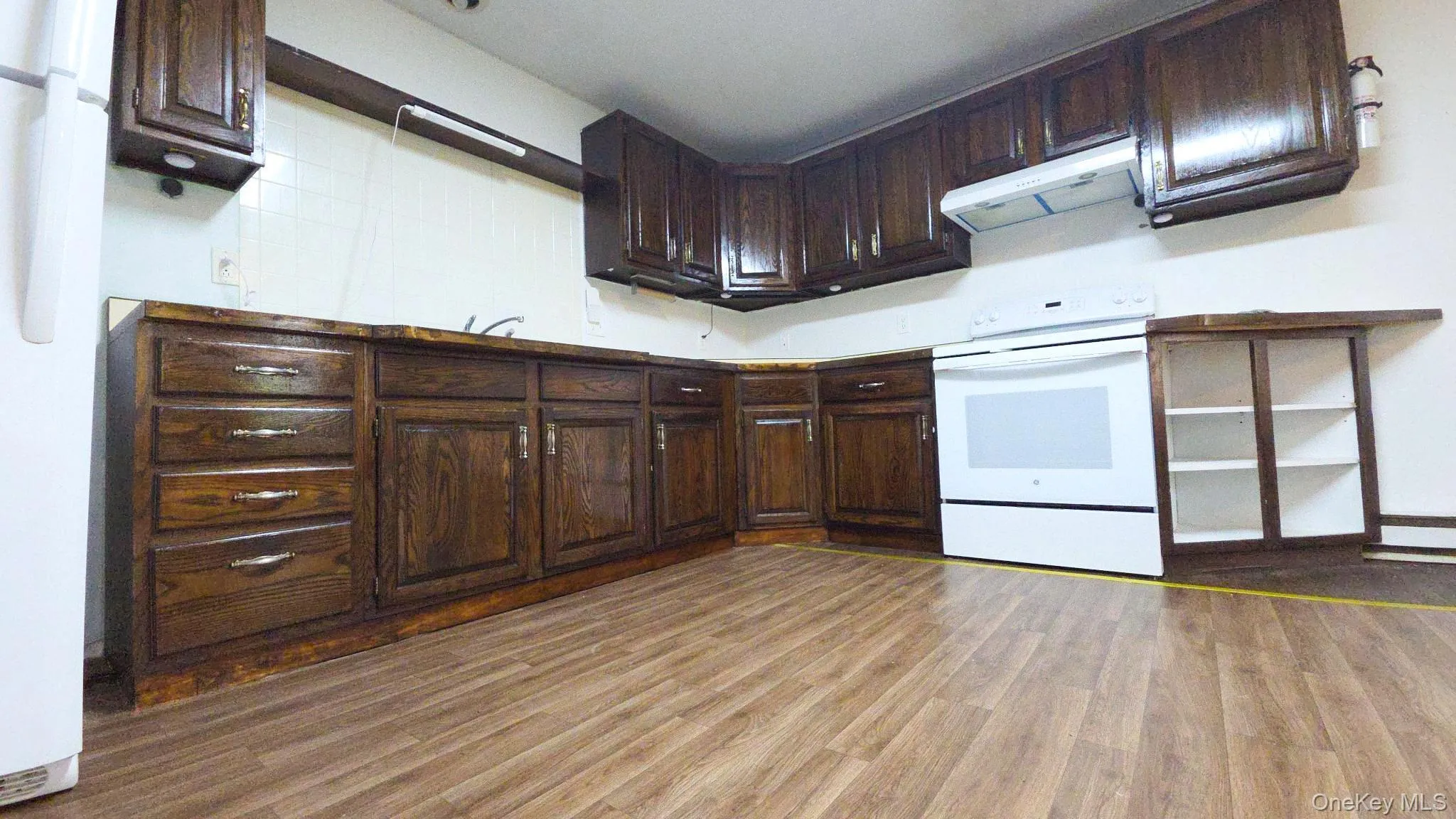 Kitchen featuring wood-finish flooring, dark wood cabinetry, a white refrigerator, and a white range with an overhead exhaust hood Kitchen featuring wood-finish flooring, dark wood cabinetry, a white refrigerator, and a white range with an overhead exhaust hood