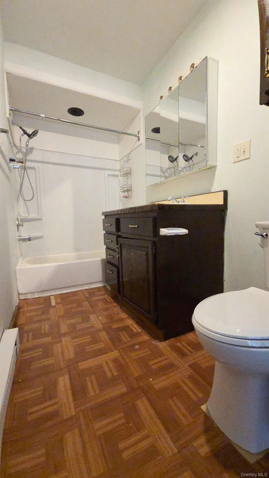 Bathroom featuring wood-finish flooring, a white bathtub with shower fixtures, a dark wood vanity with a light-colored countertop, and a triple mirrored medicine cabinet Bathroom featuring wood-finish flooring, a white bathtub with shower fixtures, a dark wood vanity with a light-colored countertop, and a triple mirrored medicine cabinet