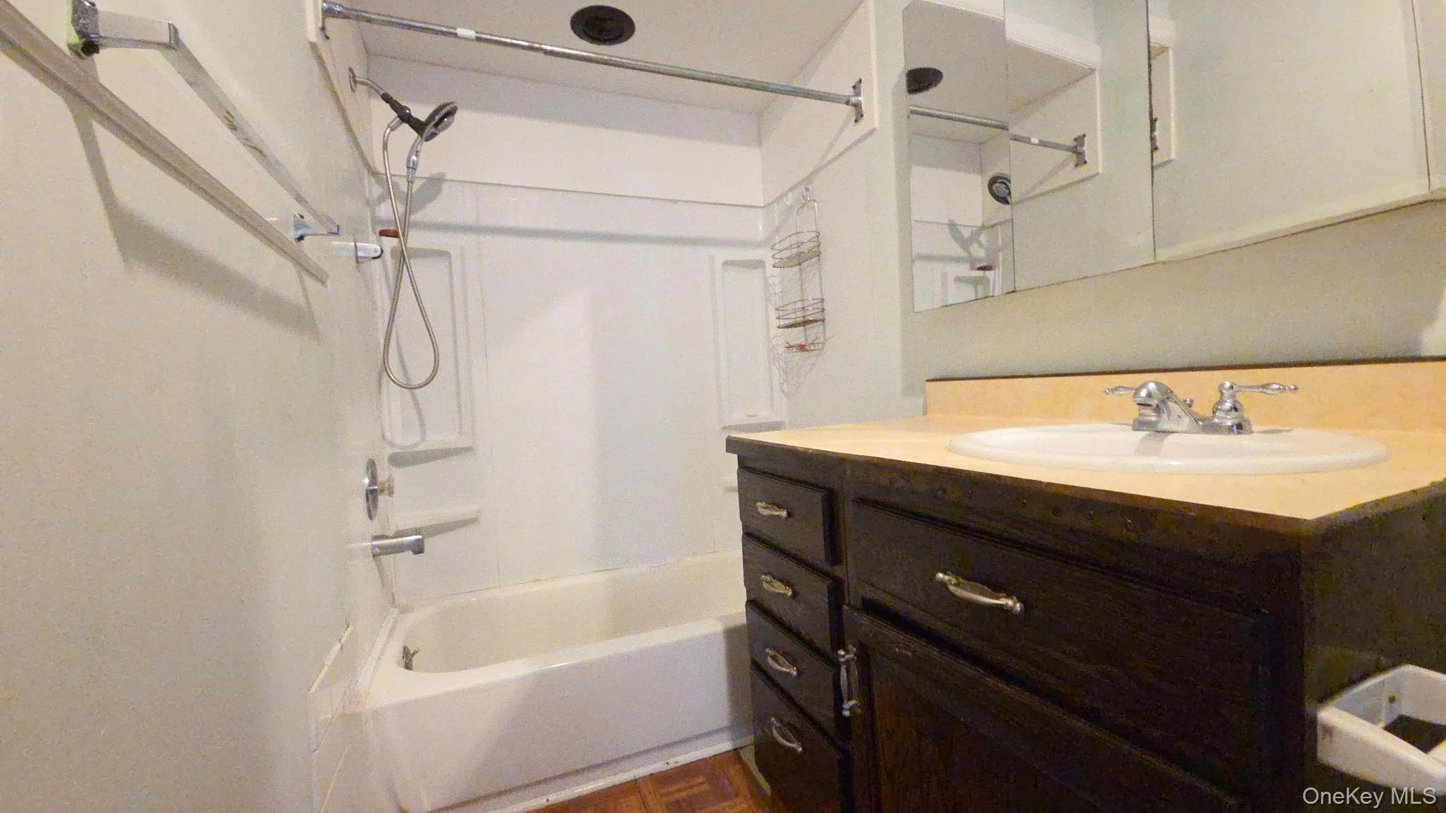 Bathroom featuring a white bathtub with shower, dark wood-finish vanity, light-toned countertop, and recessed medicine cabinet Bathroom featuring a white bathtub with shower, dark wood-finish vanity, light-toned countertop, and recessed medicine cabinet