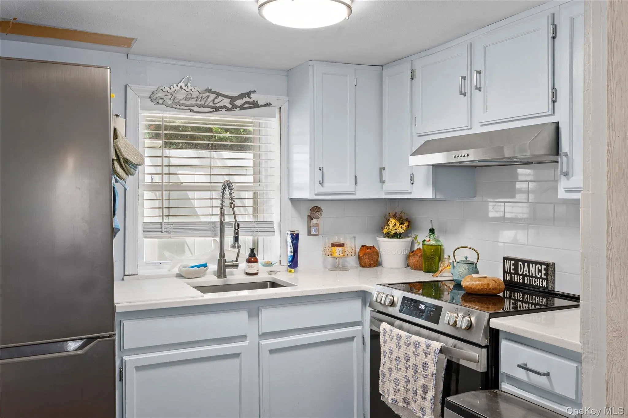 Kitchen featuring light blue cabinetry, white countertops, a stainless steel refrigerator, a stainless steel range with a flat cooktop, and a white subway tile backsplash Kitchen featuring light blue cabinetry, white countertops, a stainless steel refrigerator, a stainless steel range with a flat cooktop, and a white subway tile backsplash