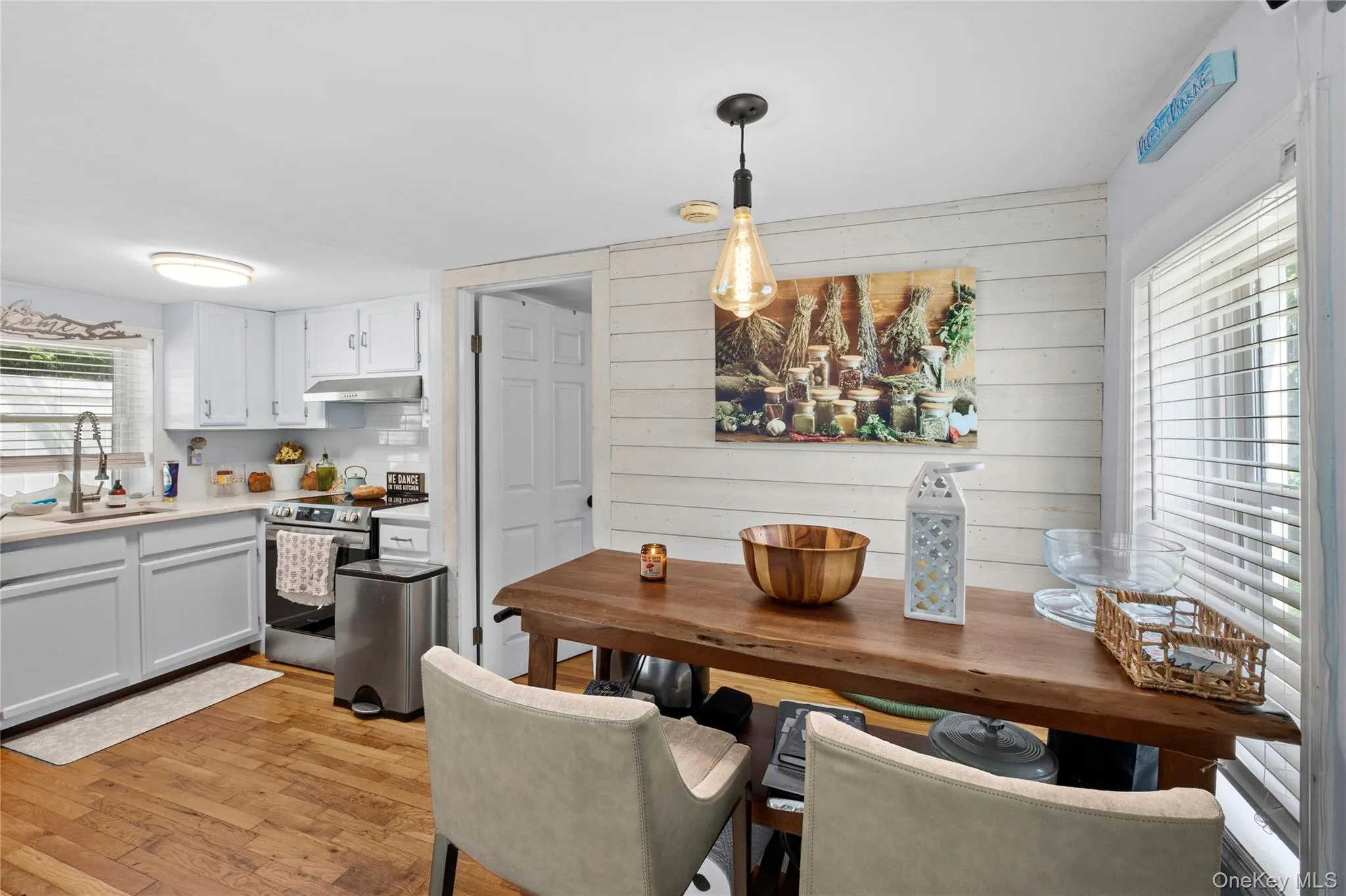 Kitchen dining area featuring a live-edge wood table, pendant lighting, wood-finish flooring, white shiplap wall, and a window with blinds Kitchen dining area featuring a live-edge wood table, pendant lighting, wood-finish flooring, white shiplap wall, and a window with blinds