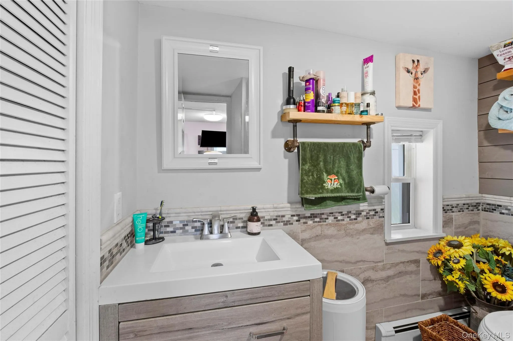 Bathroom featuring a white framed mirror, a single-handle faucet, a built-in floating shelf with a towel bar, a window with white trim, and light gray wall paint Bathroom featuring a white framed mirror, a single-handle faucet, a built-in floating shelf with a towel bar, a window with white trim, and light gray wall paint