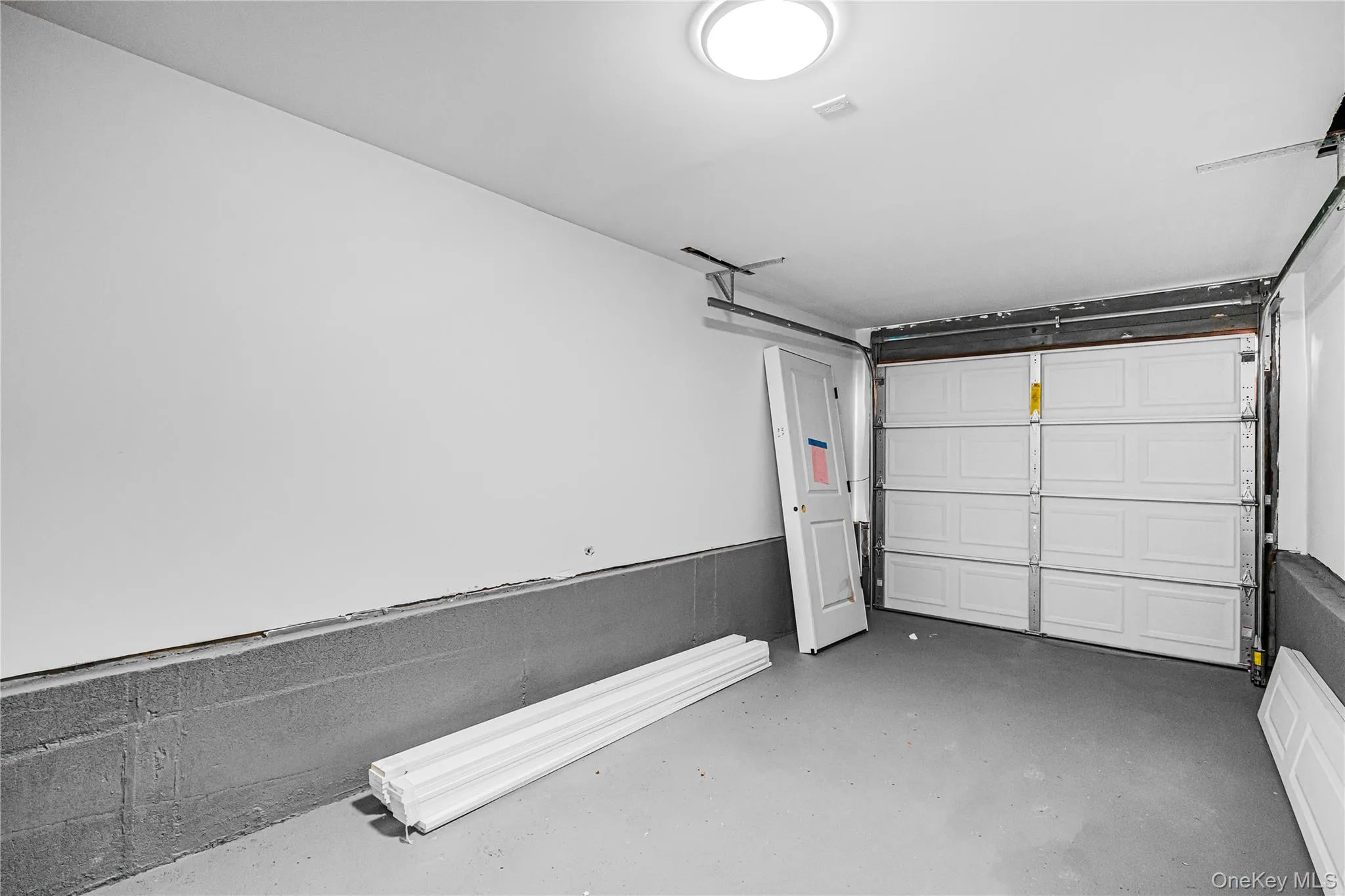 Garage interior featuring a white paneled door, gray concrete flooring, and a flush-mount ceiling light Garage interior featuring a white paneled door, gray concrete flooring, and a flush-mount ceiling light