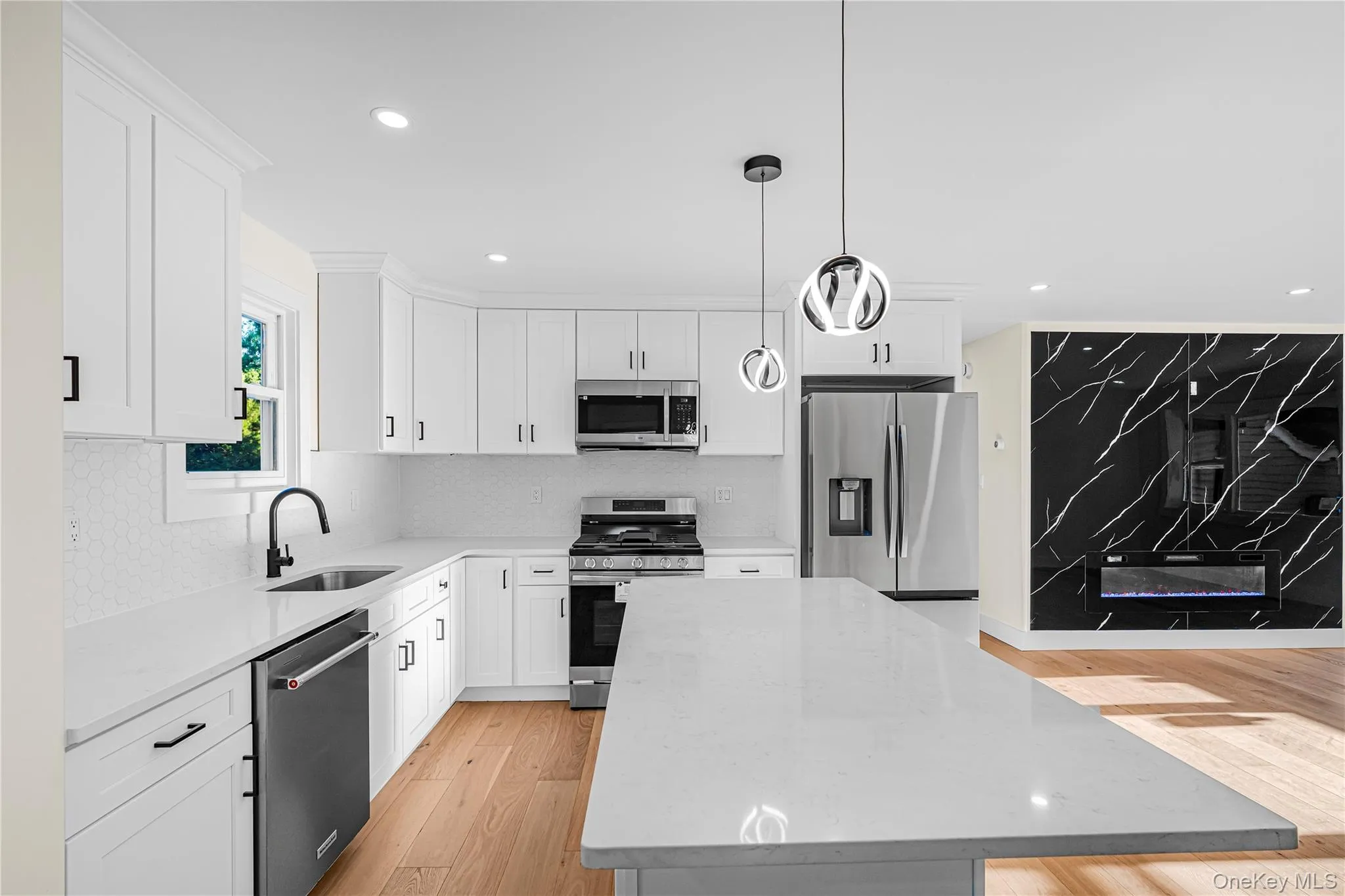 Kitchen featuring a central island with a light-toned countertop, white cabinetry with black hardware, stainless steel appliances, and a white tiled backsplash Kitchen featuring a central island with a light-toned countertop, white cabinetry with black hardware, stainless steel appliances, and a white tiled backsplash