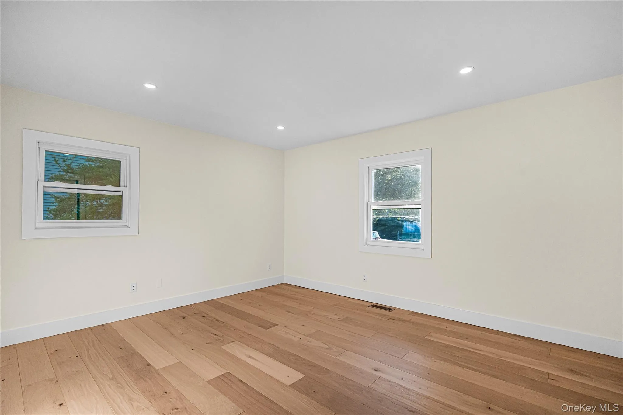 Room featuring warm-toned wood-finish flooring, light-colored walls, and recessed ceiling lighting Room featuring warm-toned wood-finish flooring, light-colored walls, and recessed ceiling lighting