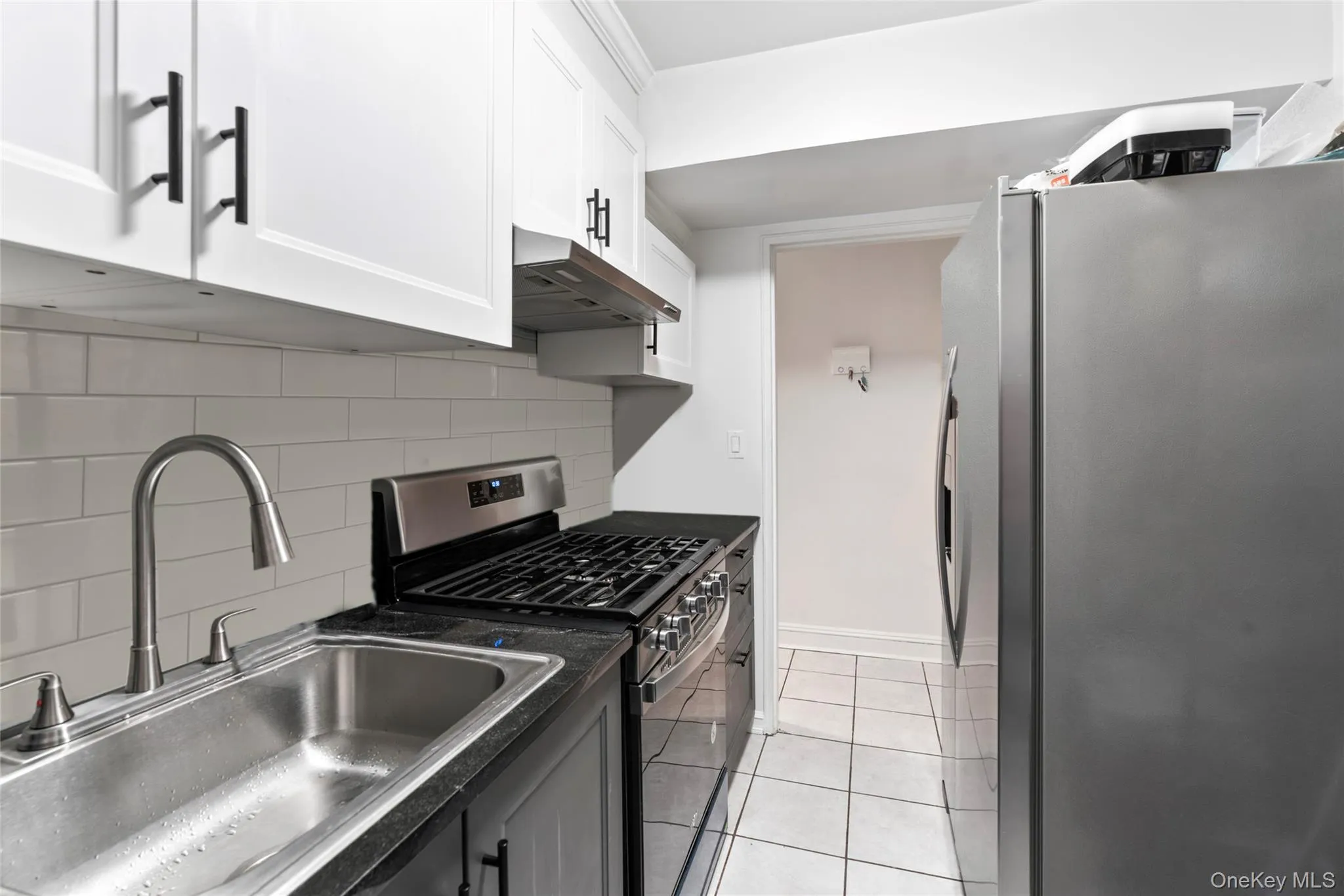 Kitchen featuring appliances with stainless steel finishes, under cabinet range hood, dark countertops, white cabinetry, and backsplash Kitchen featuring appliances with stainless steel finishes, under cabinet range hood, dark countertops, white cabinetry, and backsplash