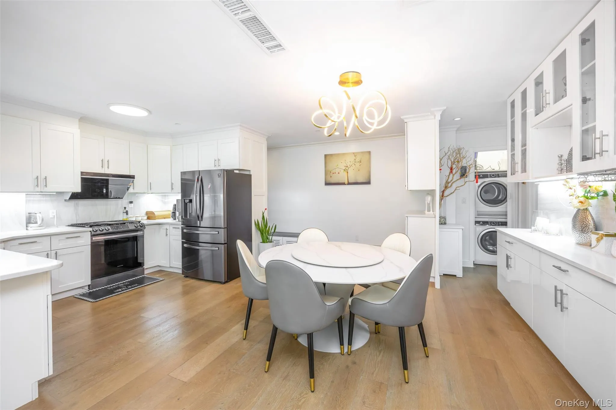 Dining room with stacked washer / dryer, light wood-style floors, ornamental molding, and a chandelier Dining room with stacked washer / dryer, light wood-style floors, ornamental molding, and a chandelier