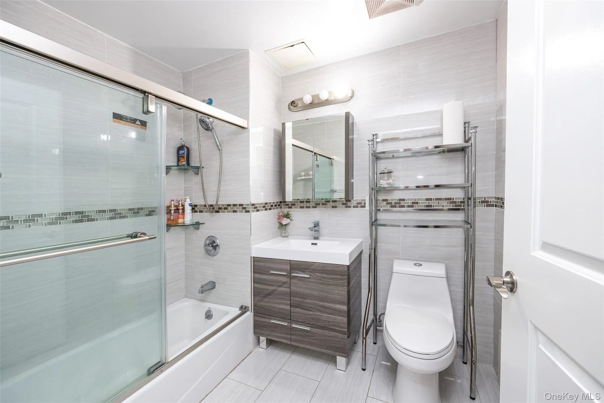 Full bath with tile walls, combined bath / shower with glass door, vanity, and light tile patterned floors Full bath with tile walls, combined bath / shower with glass door, vanity, and light tile patterned floors