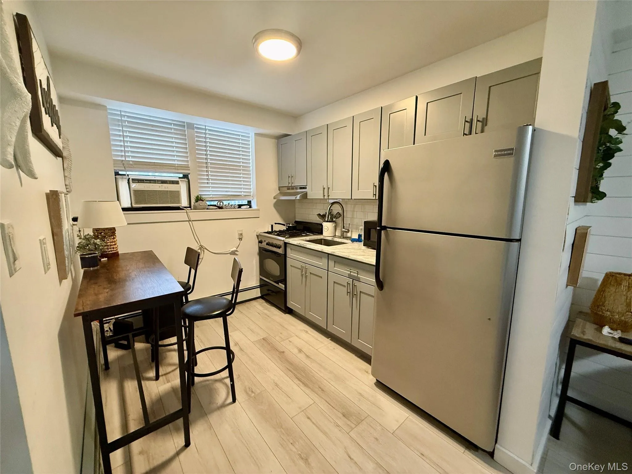 Kitchen with gray cabinets, light countertops, gas stove, freestanding refrigerator, and backsplash Kitchen with gray cabinets, light countertops, gas stove, freestanding refrigerator, and backsplash