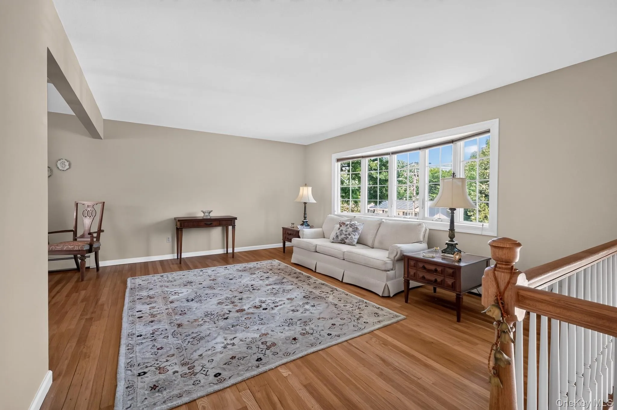 Spacious living area featuring expansive bay windows, wood-finish flooring, and a neutral color palette Spacious living area featuring expansive bay windows, wood-finish flooring, and a neutral color palette