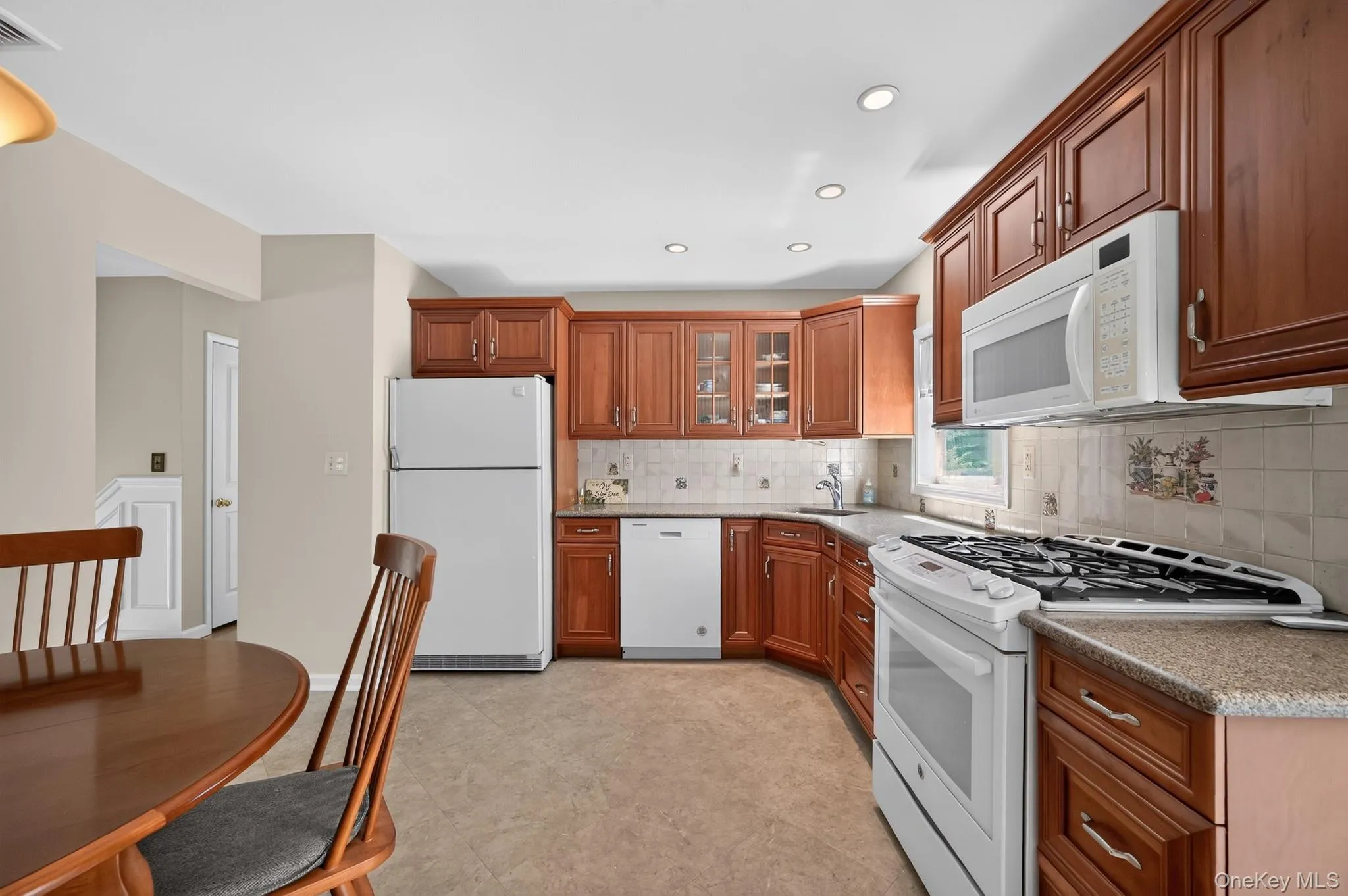 Kitchen featuring warm wood cabinetry, light-toned Corian countertops, and a full suite of white appliances including a slide in range, microwave, dish washer and refrigerator Kitchen featuring warm wood cabinetry, light-toned Corian countertops, and a full suite of white appliances including a slide in range, microwave, dish washer and refrigerator