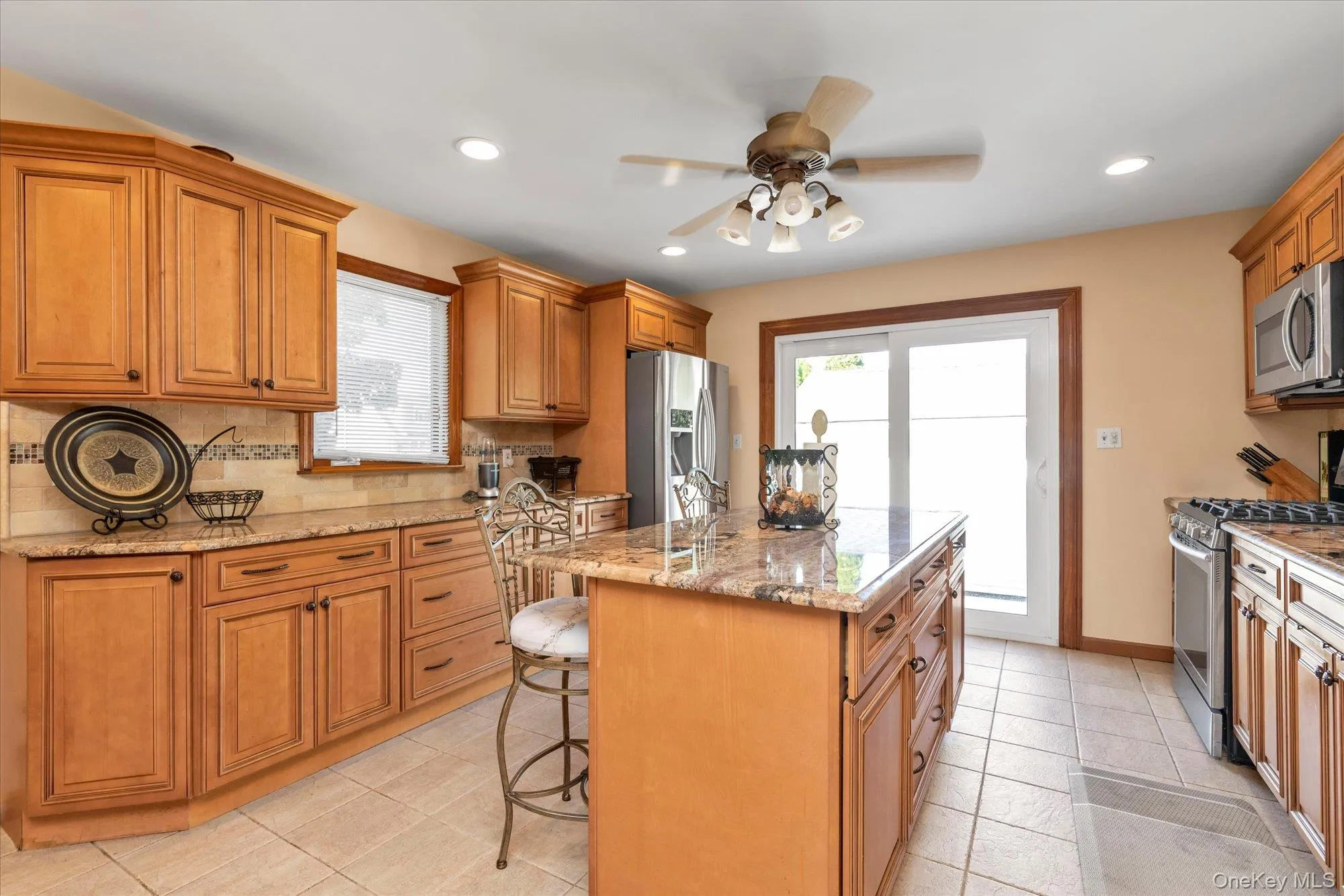 Kitchen featuring wood cabinetry, granite countertops, tile flooring, a center island, and stainless steel appliances Kitchen featuring wood cabinetry, granite countertops, tile flooring, a center island, and stainless steel appliances
