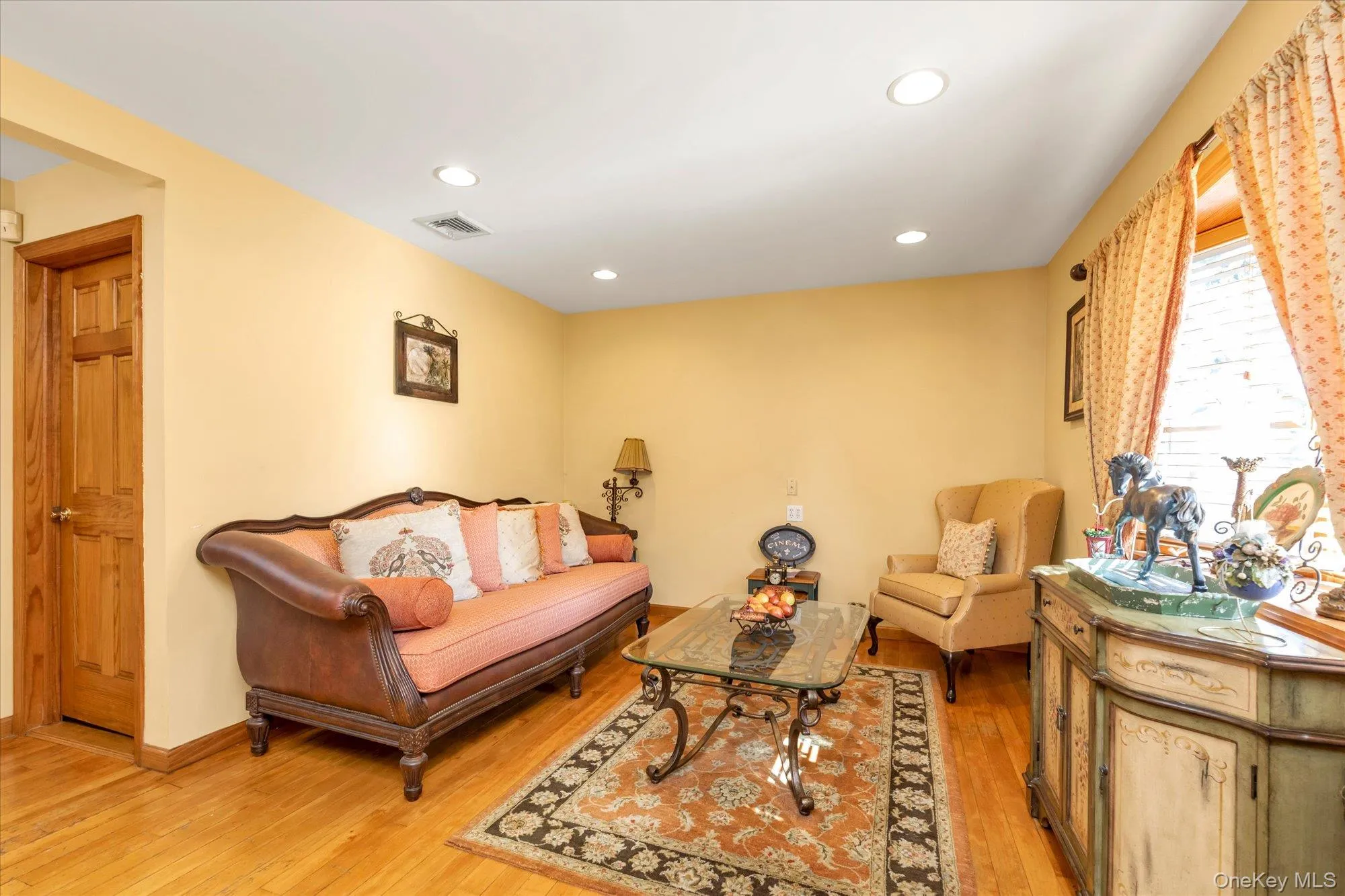 Living area featuring hardwood flooring, recessed lighting, a wooden staircase, and a doorway Living area featuring hardwood flooring, recessed lighting, a wooden staircase, and a doorway