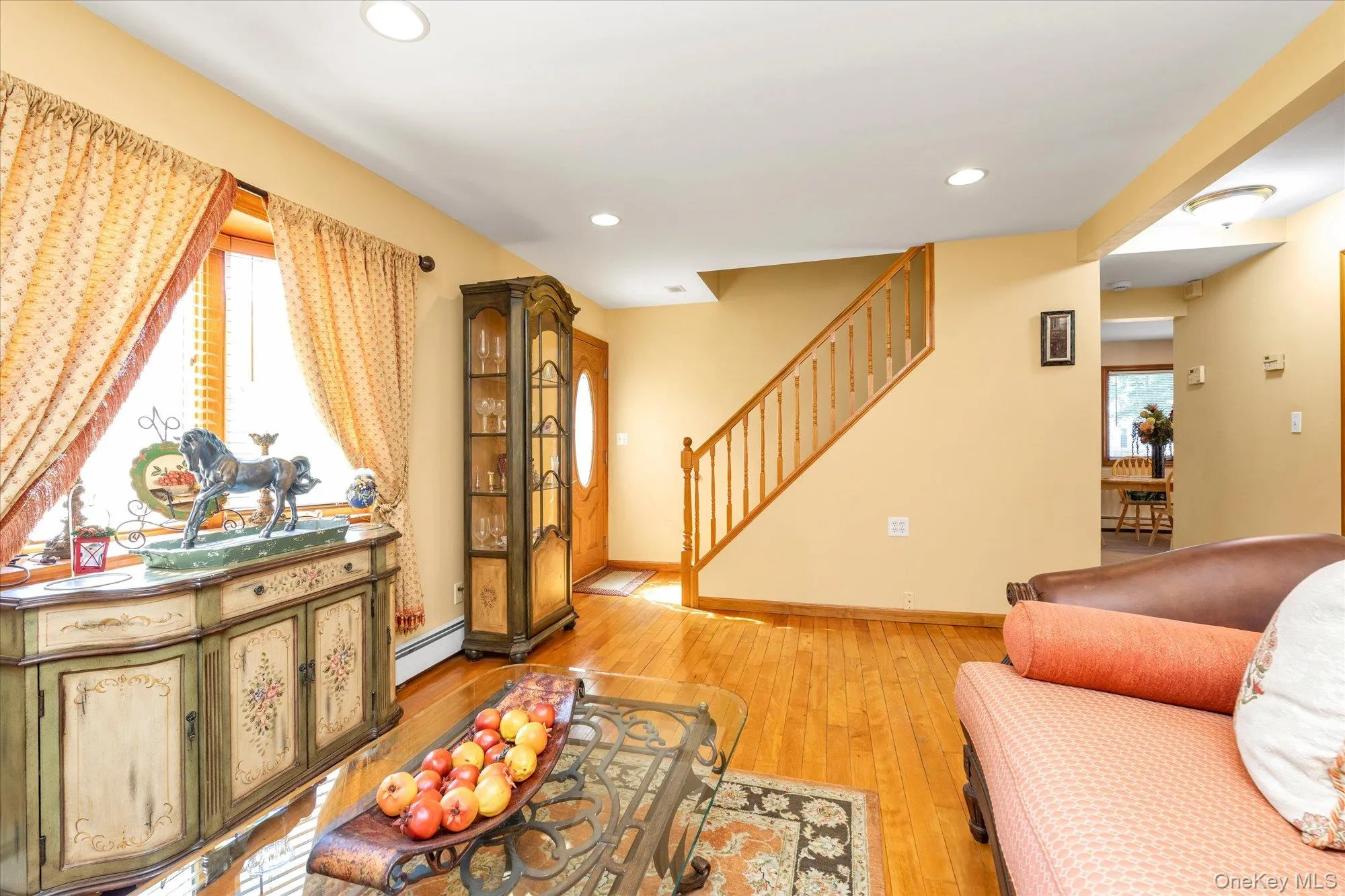 Living area featuring hardwood flooring, recessed lighting, a wooden staircase, and a doorway Living area featuring hardwood flooring, recessed lighting, a wooden staircase, and a doorway