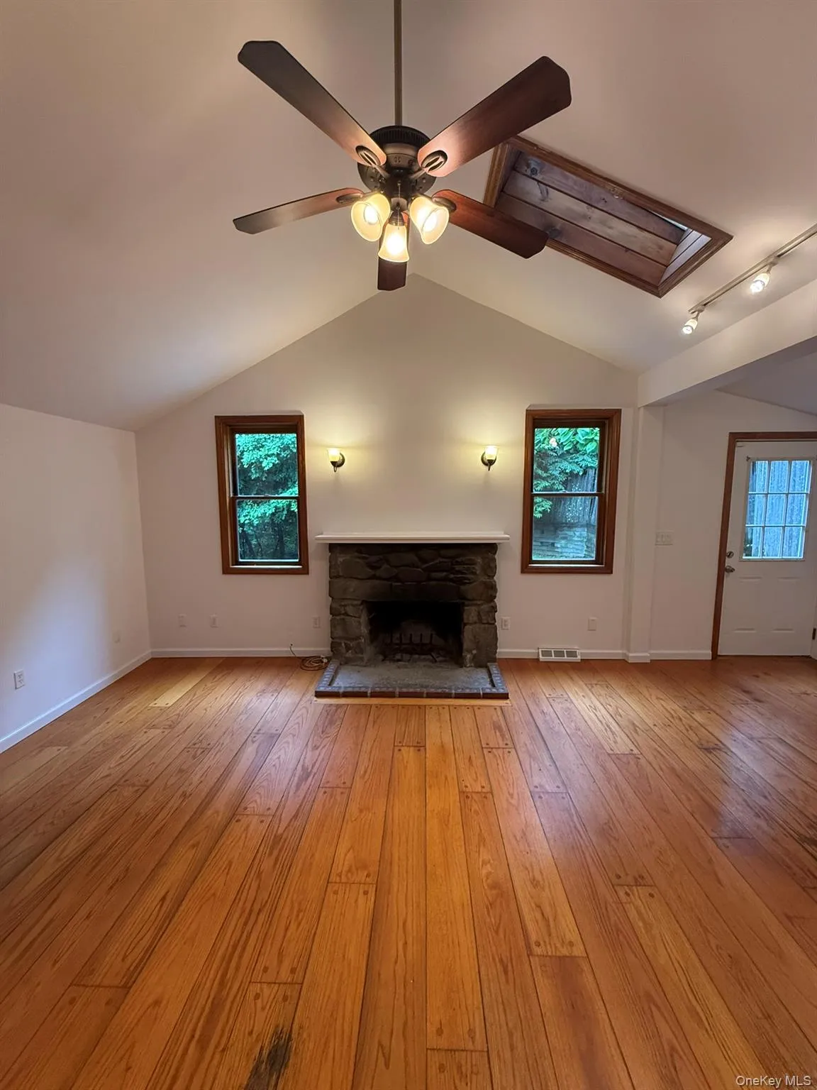 Vaulted ceiling with an exposed wood beam, wood-finish flooring, stone fireplace with hearth, and a ceiling fan with integrated lighting Vaulted ceiling with an exposed wood beam, wood-finish flooring, stone fireplace with hearth, and a ceiling fan with integrated lighting