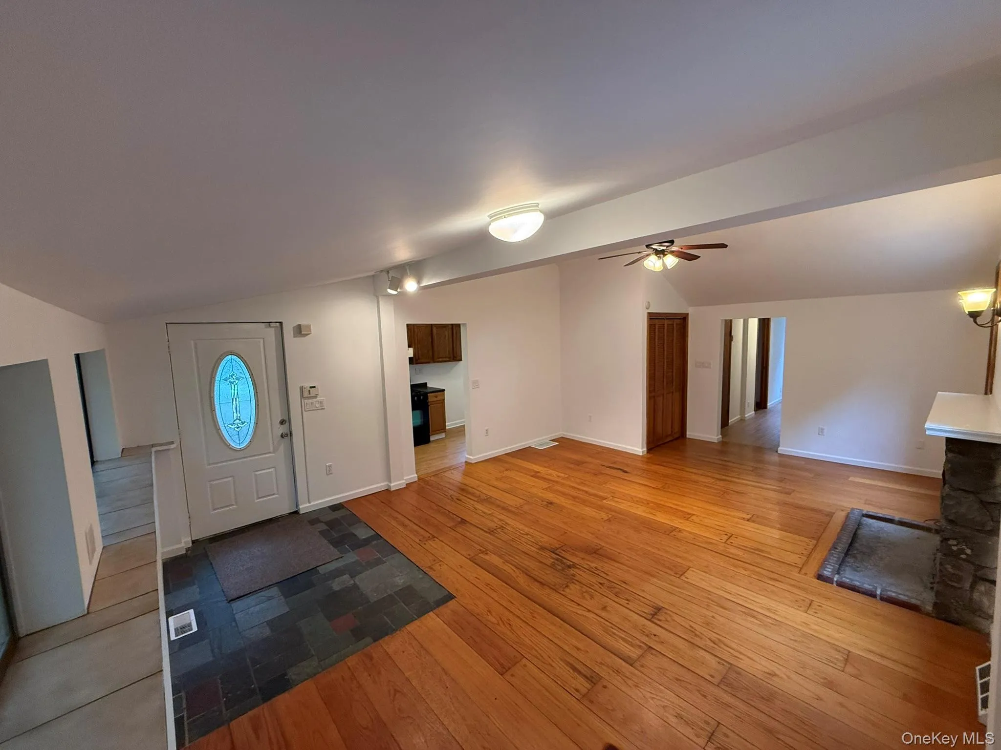 Spacious interior featuring wood-finish flooring, a stone fireplace with a white mantel, and ceiling-mounted light fixtures Spacious interior featuring wood-finish flooring, a stone fireplace with a white mantel, and ceiling-mounted light fixtures