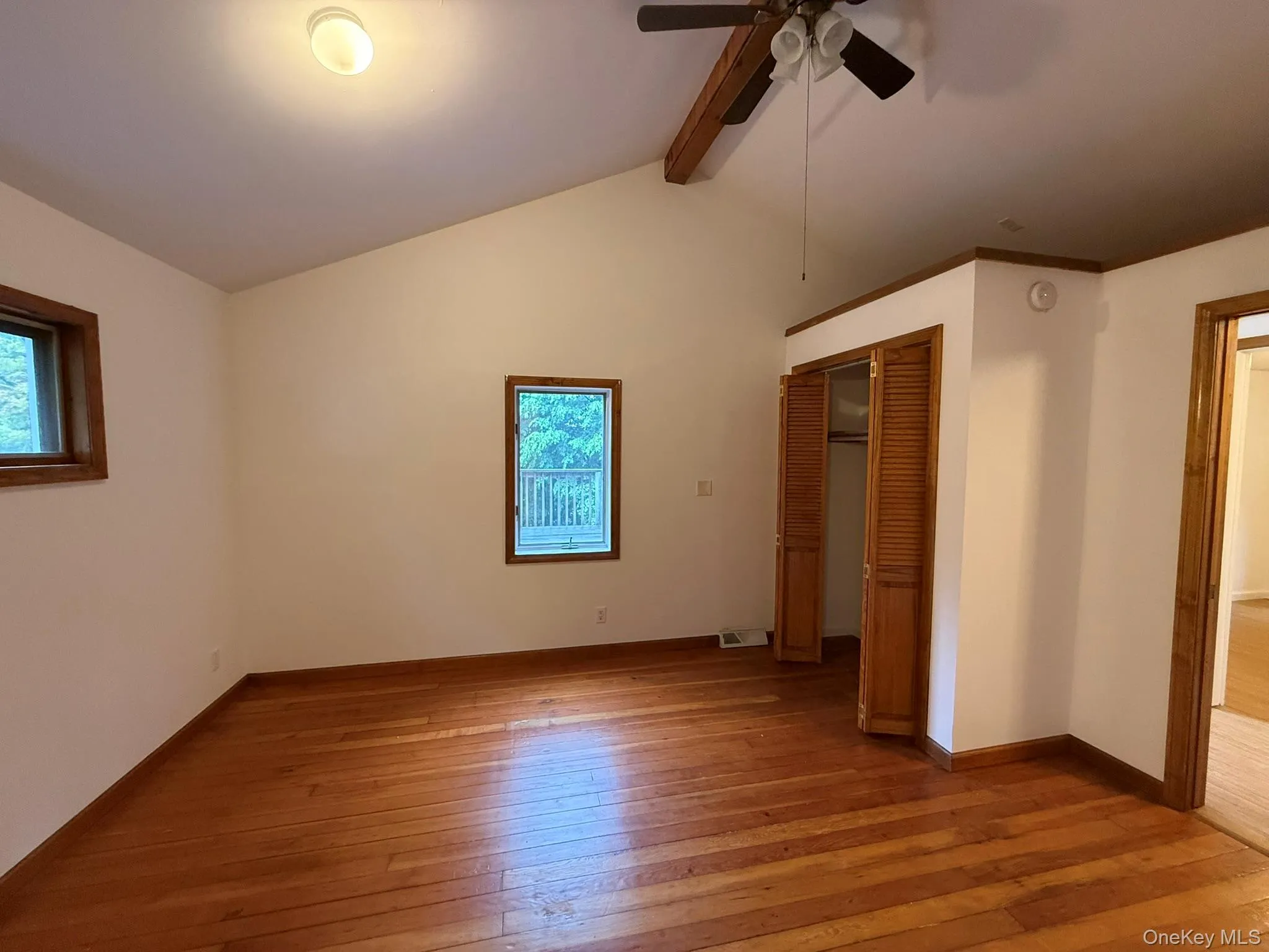 Spacious room featuring vaulted ceilings, wood-finish flooring, two windows with wood trim, and a ceiling fan Spacious room featuring vaulted ceilings, wood-finish flooring, two windows with wood trim, and a ceiling fan