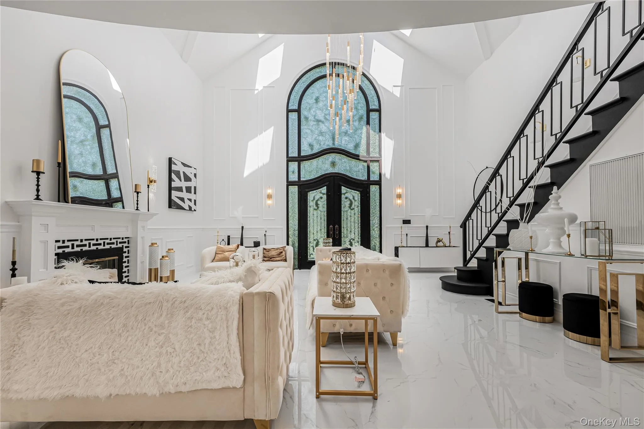 Living room featuring a decorative wall, marble tiled floors, high vaulted ceiling, stairs, and a chandelier Living room featuring a decorative wall, marble tiled floors, high vaulted ceiling, stairs, and a chandelier