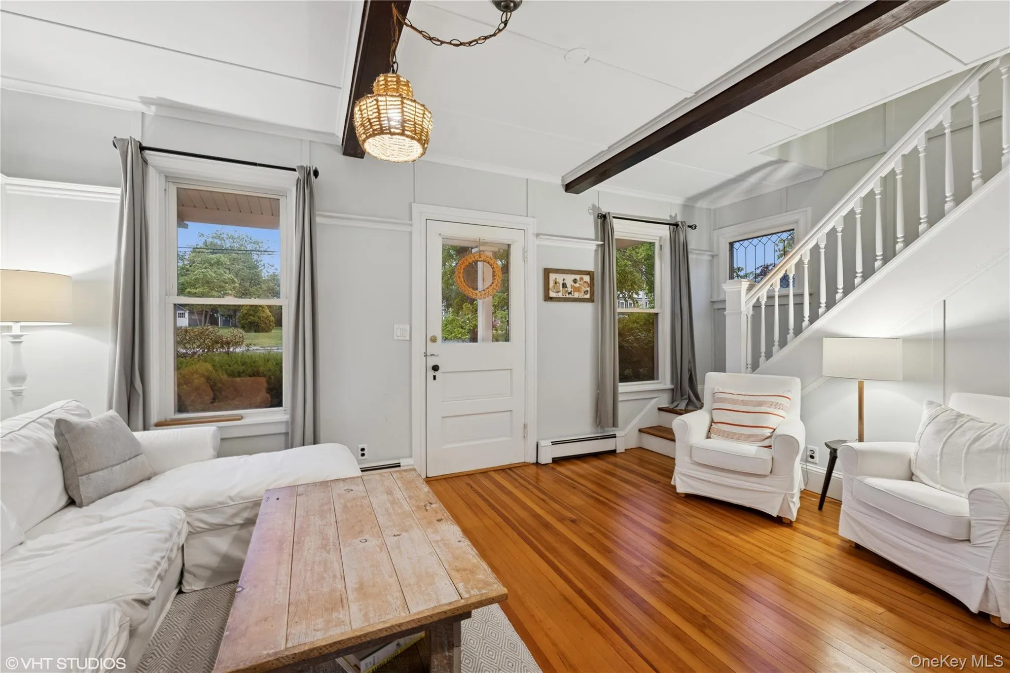Living area featuring a baseboard heating unit, stairway, wood finished floors, beamed ceiling, and a chandelier Living area featuring a baseboard heating unit, stairway, wood finished floors, beamed ceiling, and a chandelier