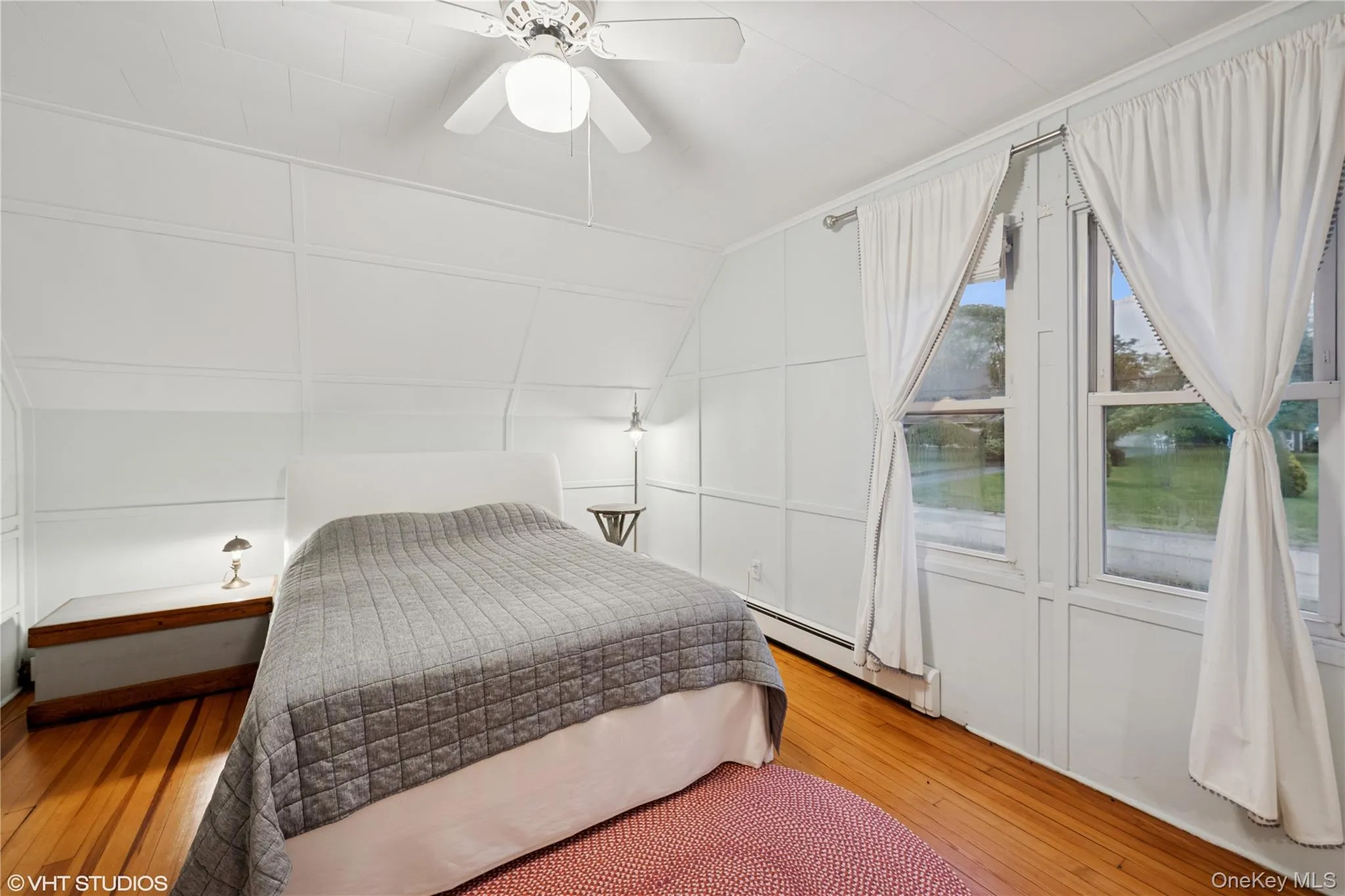 Bedroom featuring a decorative wall, light wood finished floors, baseboard heating, vaulted ceiling, and ceiling fan Bedroom featuring a decorative wall, light wood finished floors, baseboard heating, vaulted ceiling, and ceiling fan