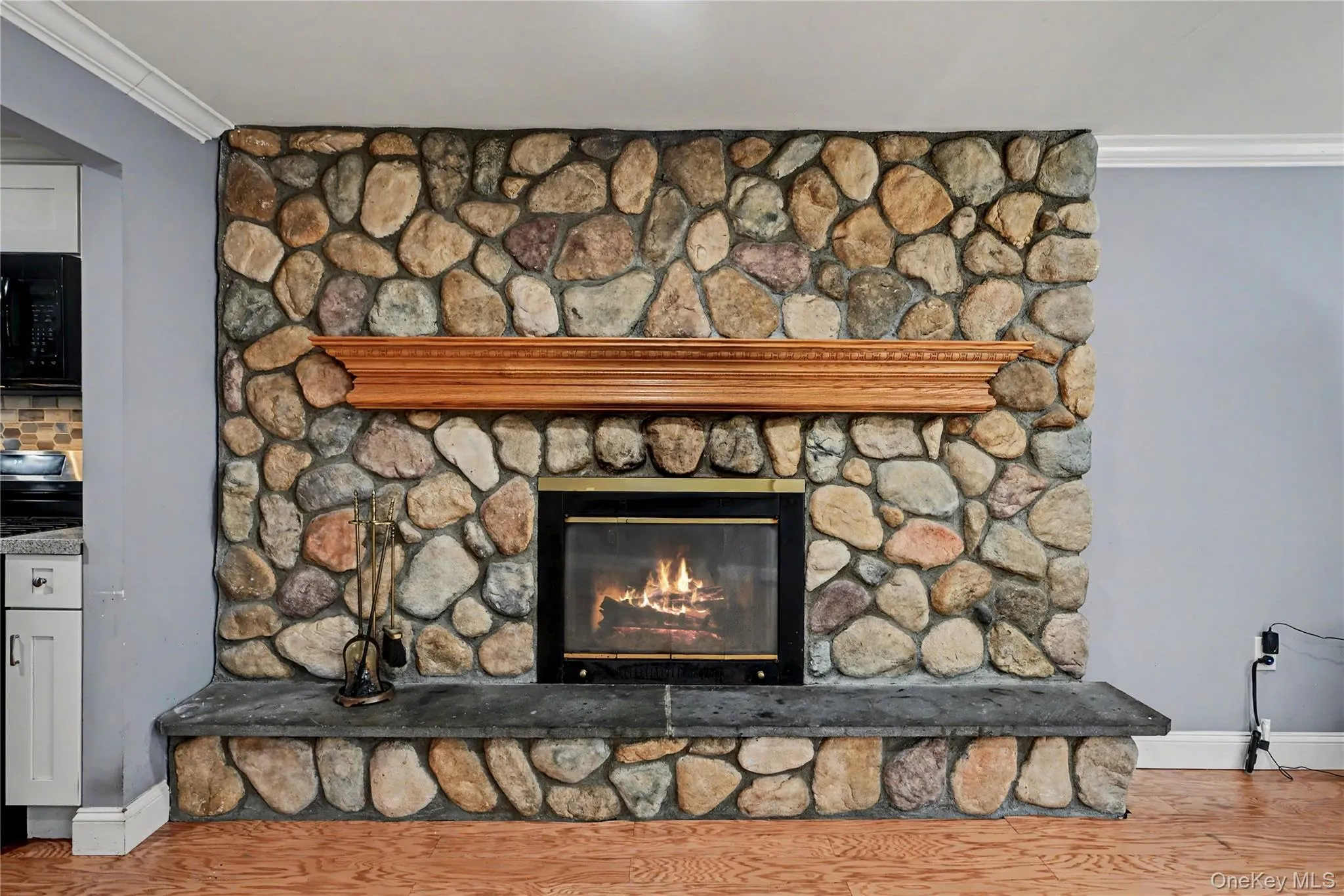 Stone fireplace with a prominent wood mantel, black firebox, and a hearth featuring stone and a dark stone slab. Stone fireplace with a prominent wood mantel, black firebox, and a hearth featuring stone and a dark stone slab.