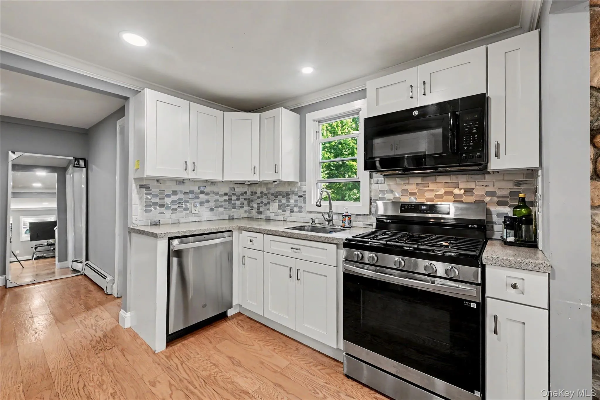 Modern kitchen featuring white shaker cabinetry, stainless steel appliances, stone countertops, and a mosaic tile backsplash. Modern kitchen featuring white shaker cabinetry, stainless steel appliances, stone countertops, and a mosaic tile backsplash.