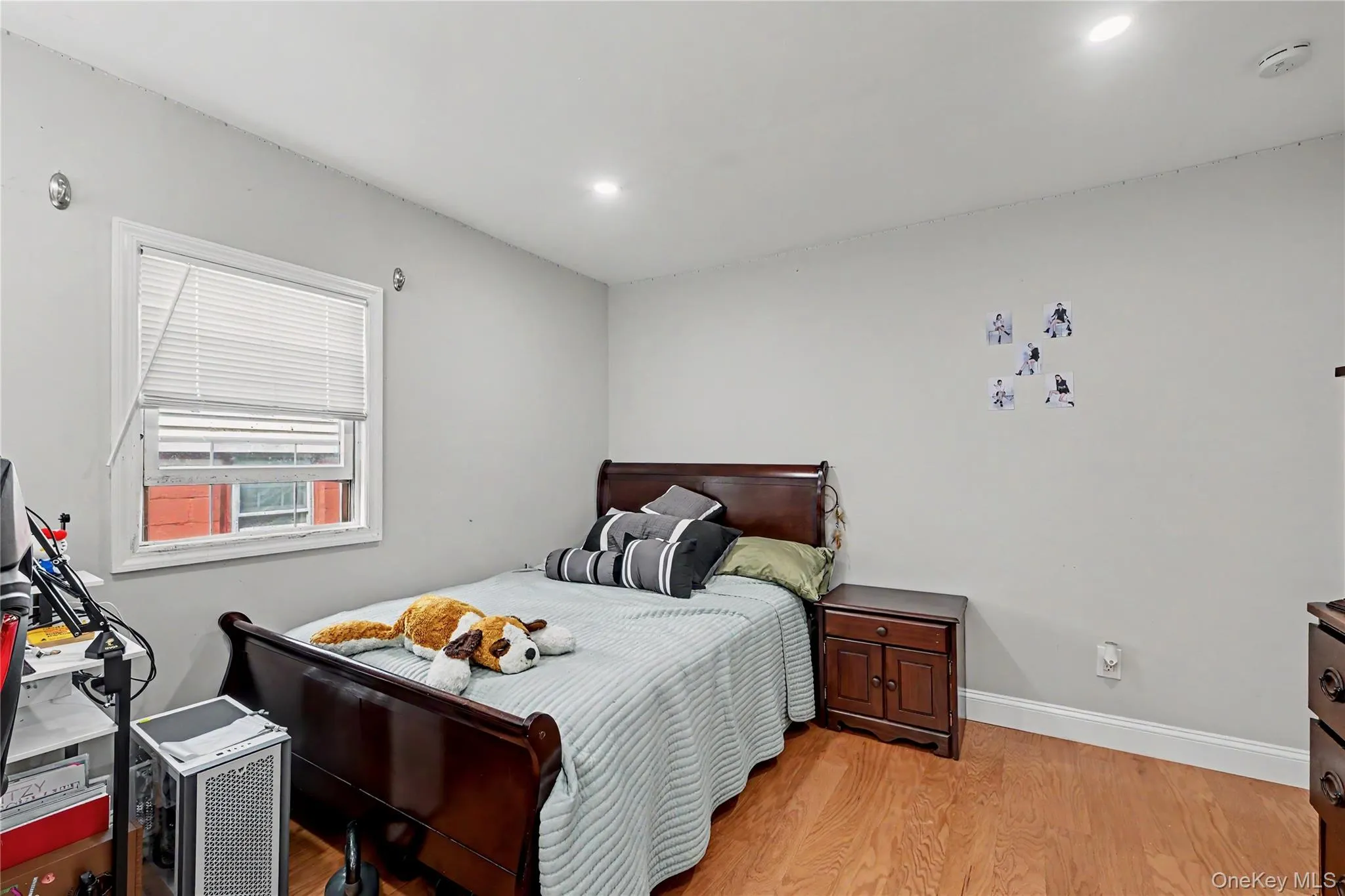 Bedroom featuring a window with blinds, wood-finish flooring, recessed lighting, and light gray wall paint. Bedroom featuring a window with blinds, wood-finish flooring, recessed lighting, and light gray wall paint.