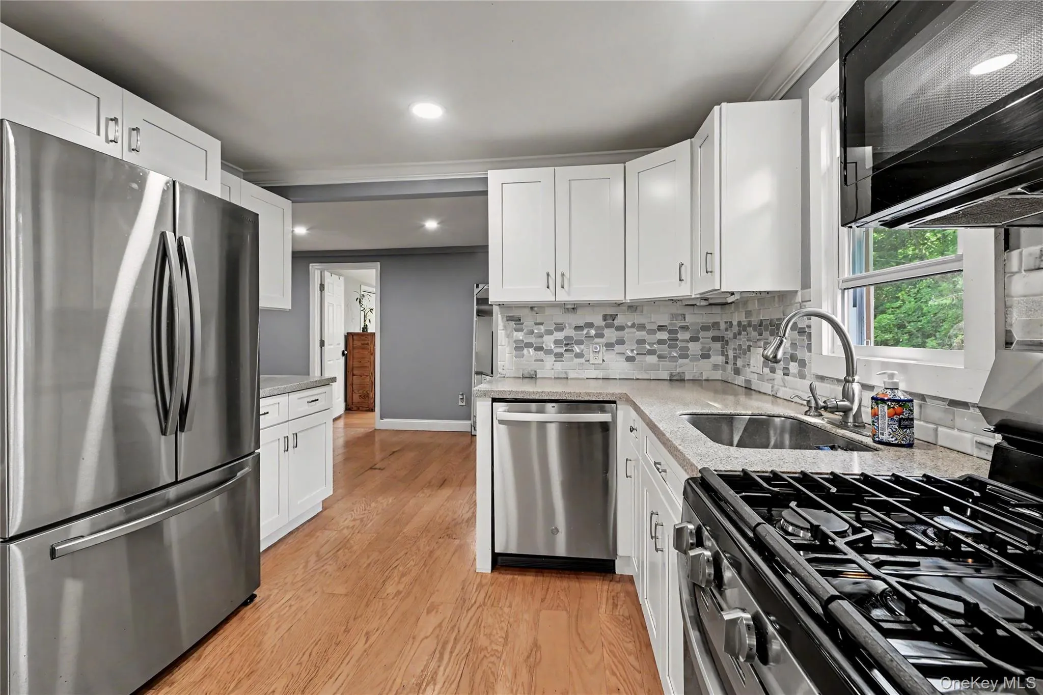 Kitchen with wood-finish flooring featuring white cabinetry, stainless steel appliances, a tile backsplash, and recessed lighting. Kitchen with wood-finish flooring featuring white cabinetry, stainless steel appliances, a tile backsplash, and recessed lighting.