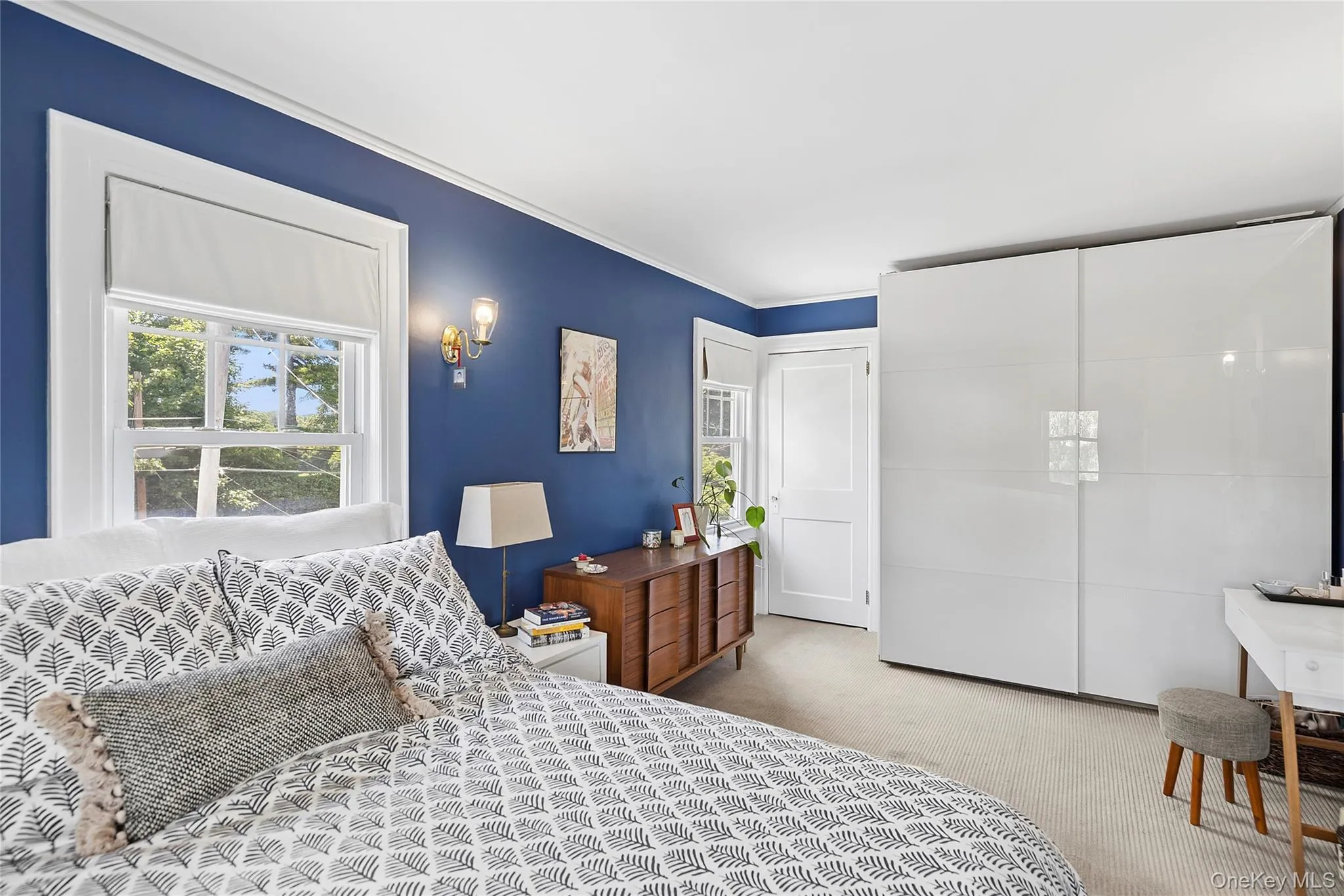 Bedroom featuring a window with white trim, a built-in wall sconce, a light-colored carpet, and a white sliding wardrobe system Bedroom featuring a window with white trim, a built-in wall sconce, a light-colored carpet, and a white sliding wardrobe system