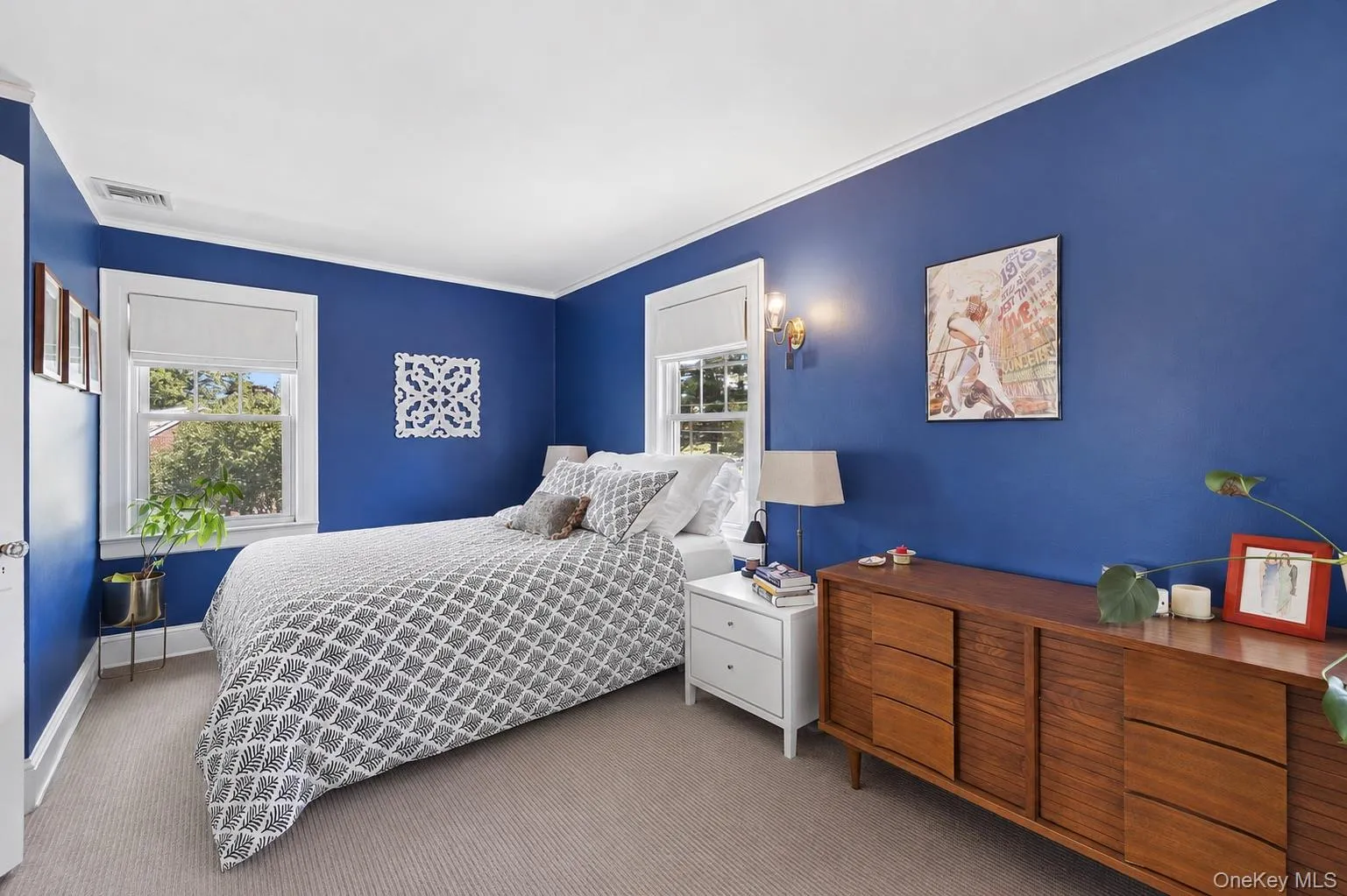 Carpeted room featuring two double-hung windows with white trim, a built-in wall sconce, and crown molding Carpeted room featuring two double-hung windows with white trim, a built-in wall sconce, and crown molding