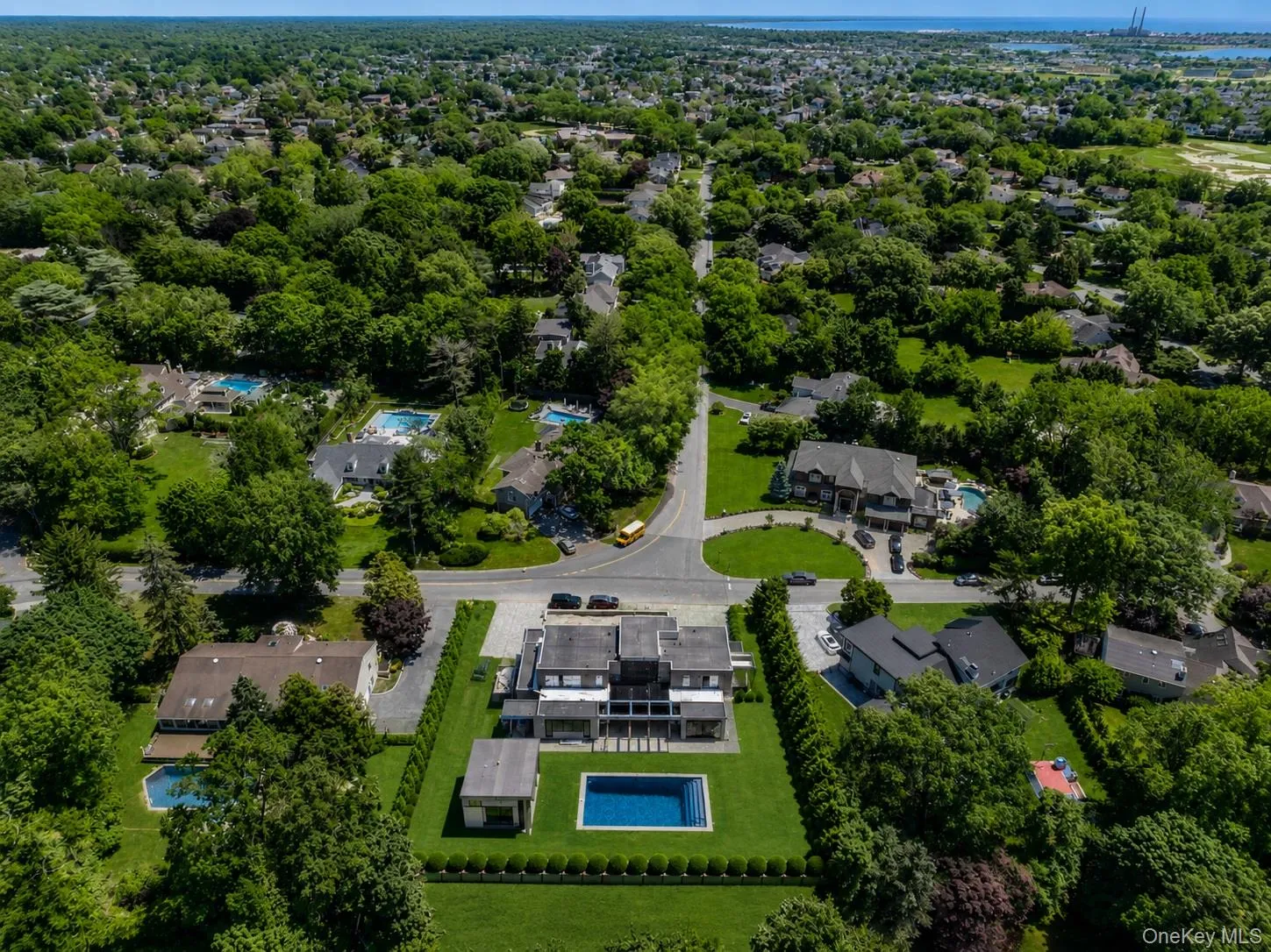 Modern residential property featuring a rectangular pool, a separate outbuilding, manicured grounds, and a circular driveway Modern residential property featuring a rectangular pool, a separate outbuilding, manicured grounds, and a circular driveway
