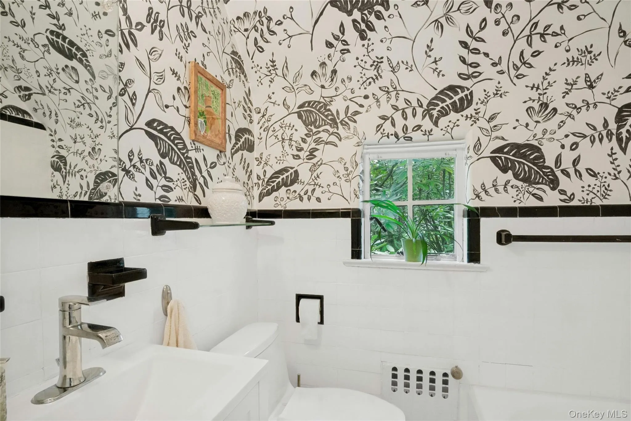 Bathroom featuring white wall tile, black trim, and botanical-patterned wallpaper Bathroom featuring white wall tile, black trim, and botanical-patterned wallpaper
