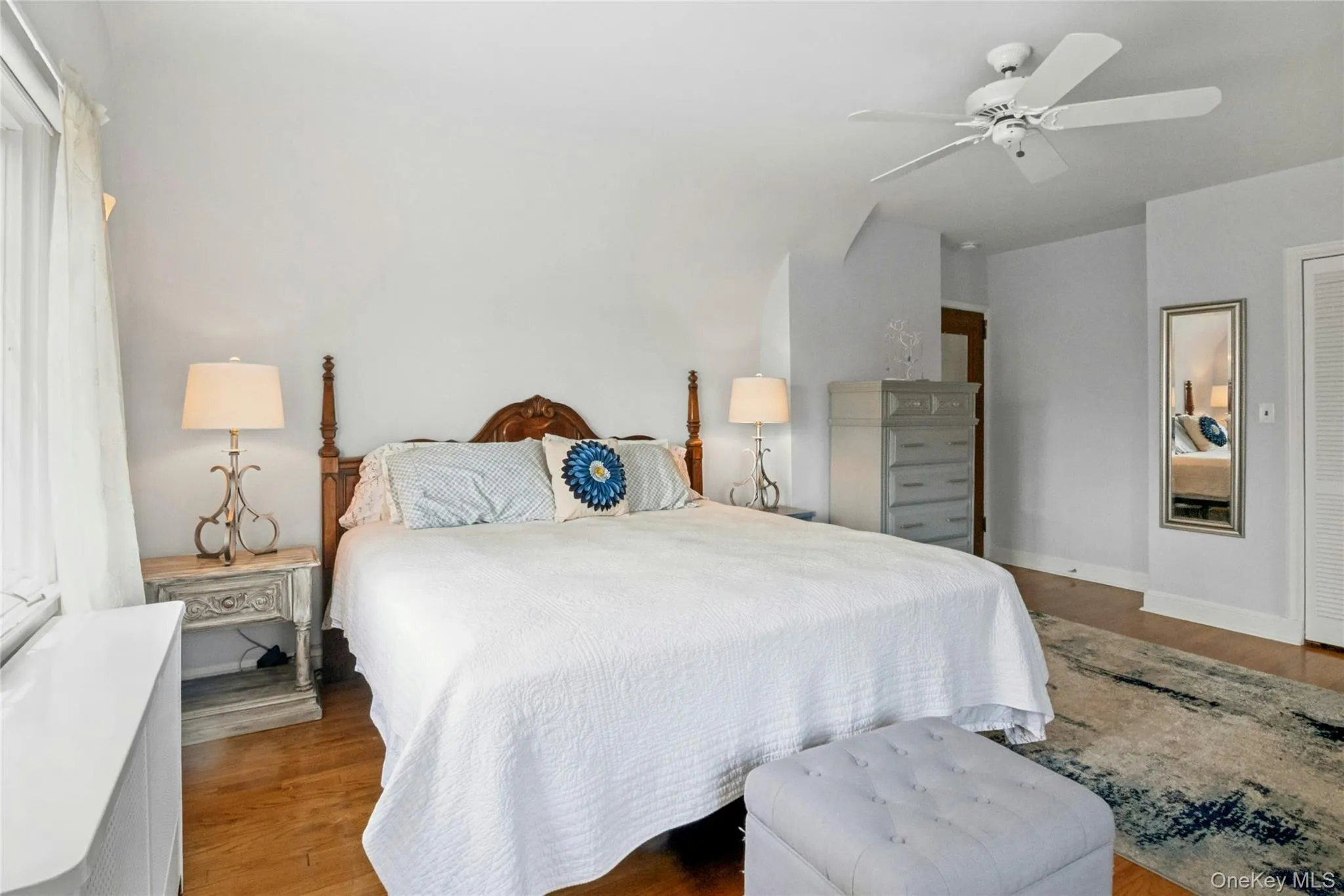 Bedroom featuring wood-finish flooring, a white ceiling fan with integrated lighting, and a window with white window treatments Bedroom featuring wood-finish flooring, a white ceiling fan with integrated lighting, and a window with white window treatments