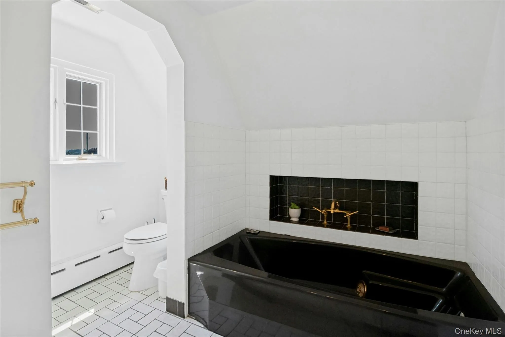Bathroom featuring a black soaking tub and shower with a built-in shelf, white subway tile surround, and a brass tub filler Bathroom featuring a black soaking tub and shower with a built-in shelf, white subway tile surround, and a brass tub filler