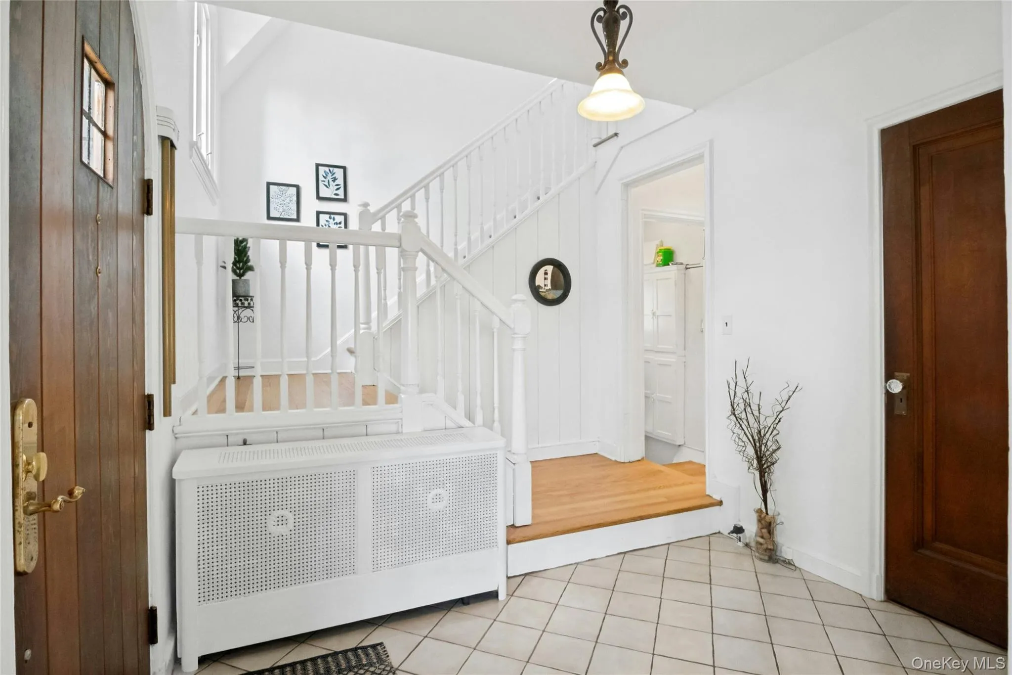Foyer featuring a light-colored tile floor, a wood-finish entry door with a window, a white staircase with wood-finish treads, and a white radiator cover Foyer featuring a light-colored tile floor, a wood-finish entry door with a window, a white staircase with wood-finish treads, and a white radiator cover