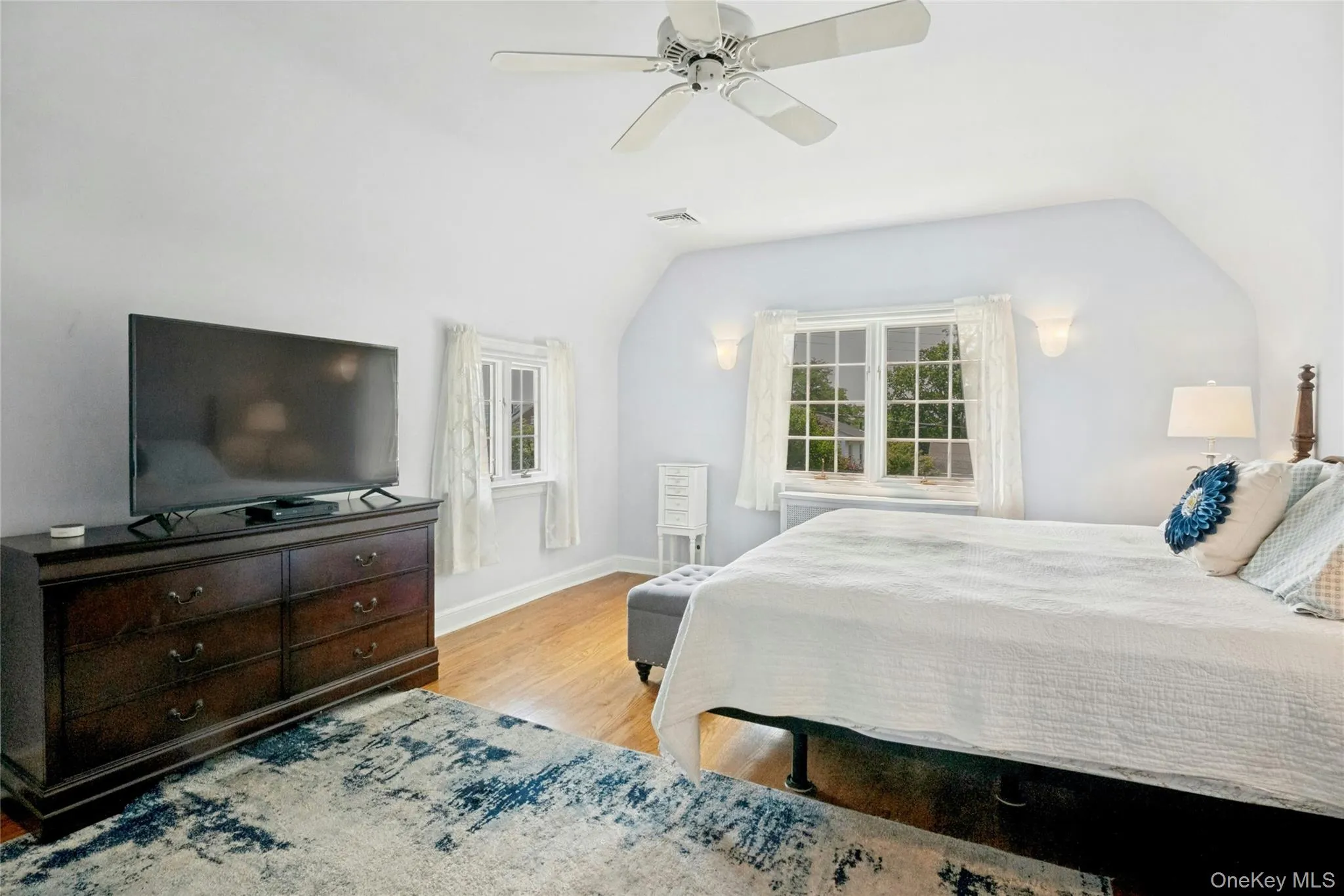Vaulted ceiling bedroom featuring wood-finish flooring, a ceiling fan, and multiple windows for abundant natural light Vaulted ceiling bedroom featuring wood-finish flooring, a ceiling fan, and multiple windows for abundant natural light