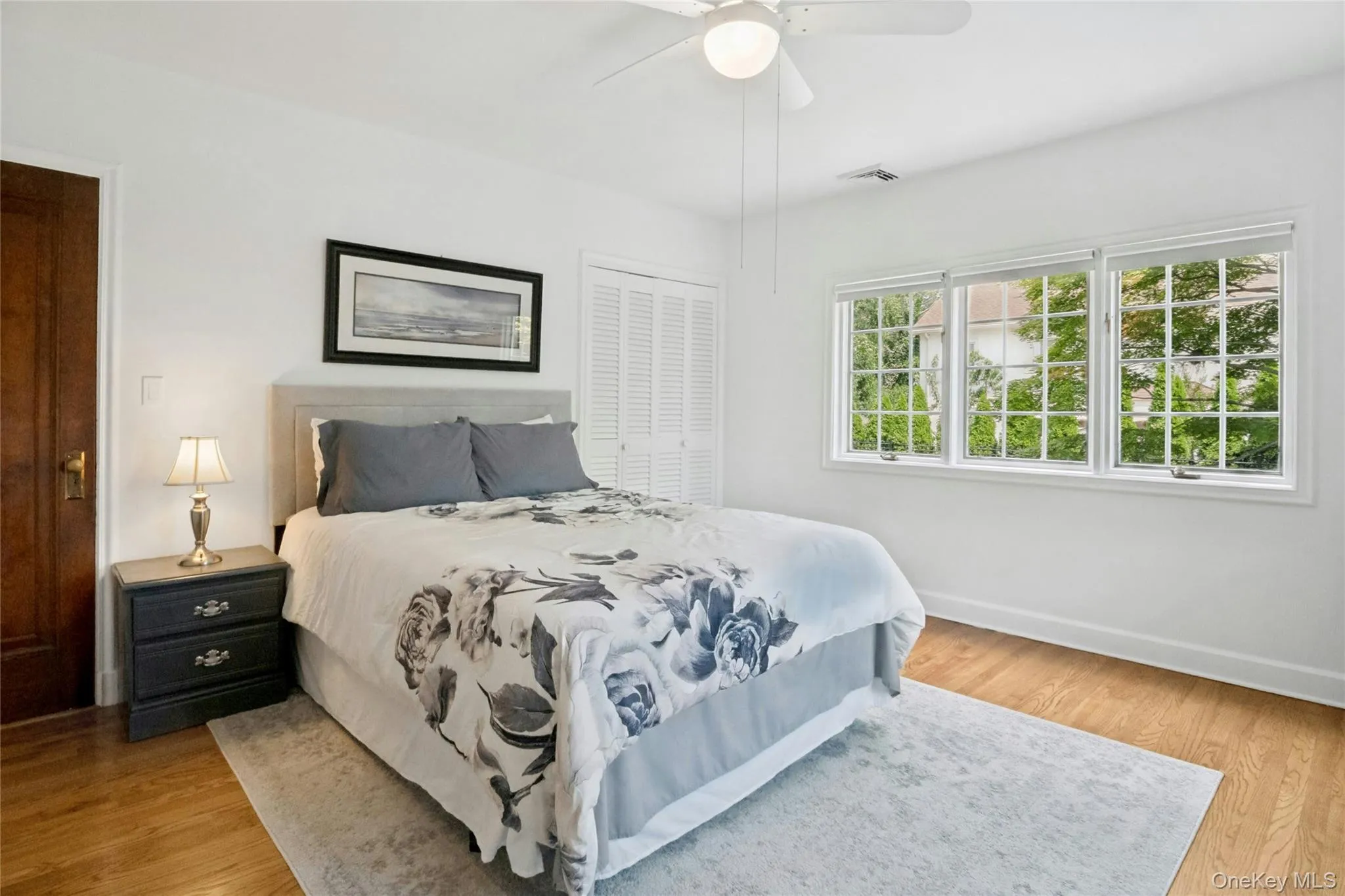 Bright bedroom featuring wood-finish flooring, a white ceiling fan, and white walls Bright bedroom featuring wood-finish flooring, a white ceiling fan, and white walls