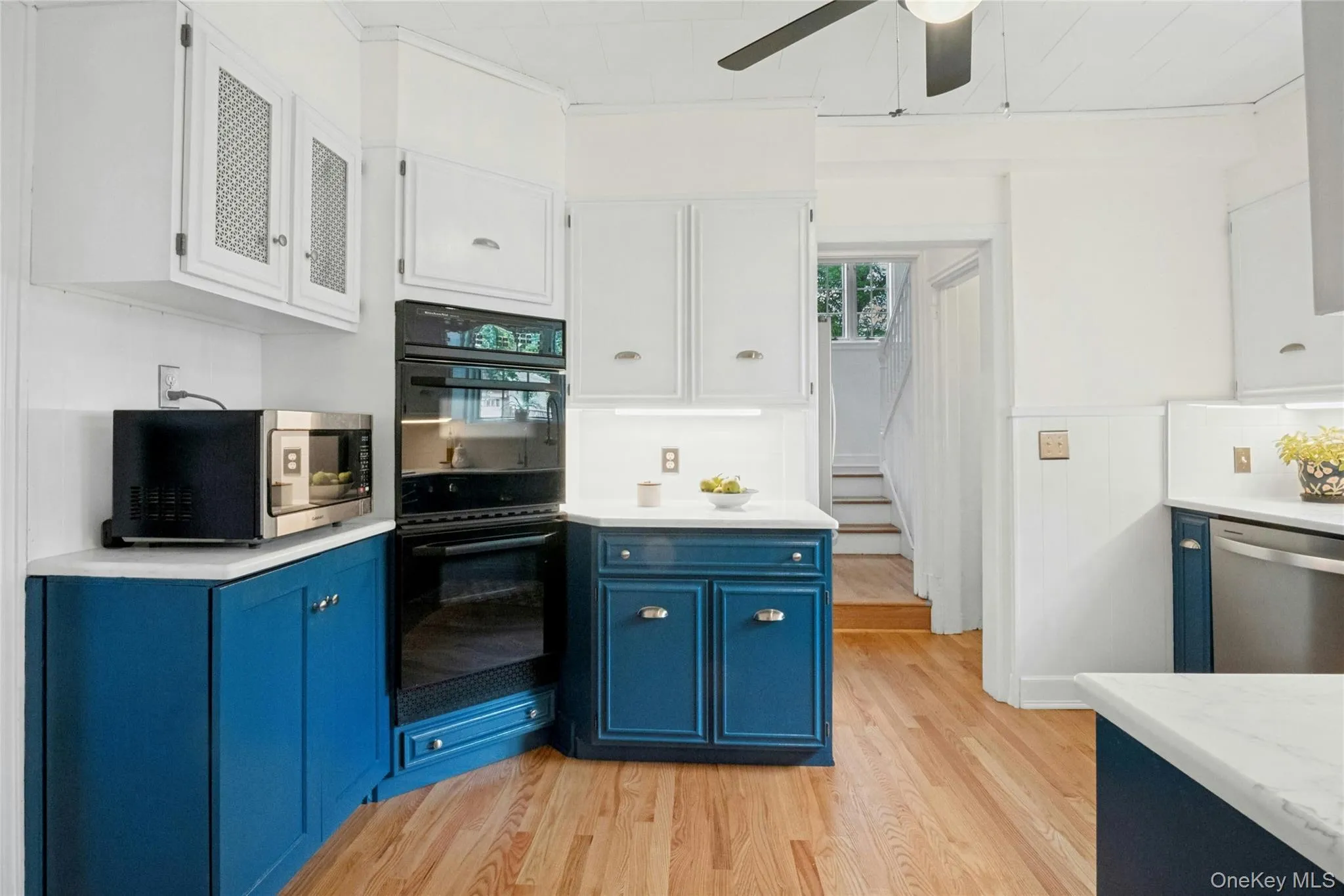 Kitchen featuring wood-finish flooring, two-tone cabinetry with white upper and blue lower cabinets, light-colored countertops, and a built-in wall oven Kitchen featuring wood-finish flooring, two-tone cabinetry with white upper and blue lower cabinets, light-colored countertops, and a built-in wall oven